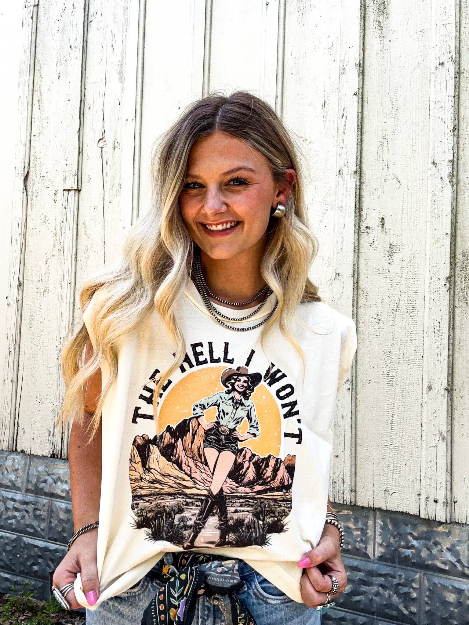Woman wearing a graphic t-shirt with a design and text, standing against a wooden fence.