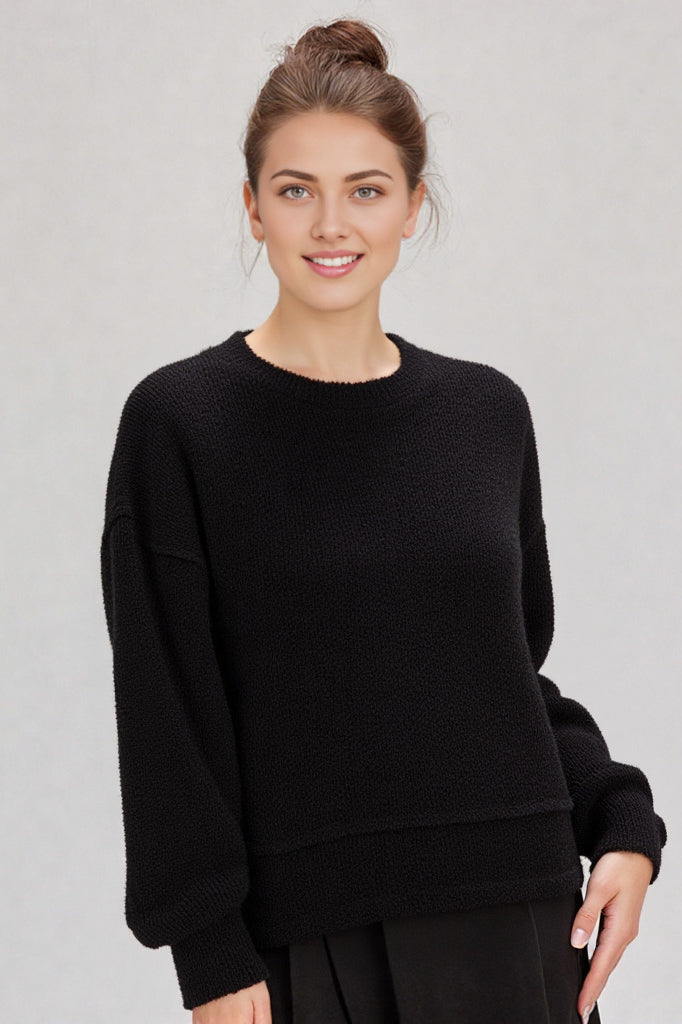 Woman in a black round-neck textured knit oversized top with drop shoulders and long sleeves, relaxed fit.”