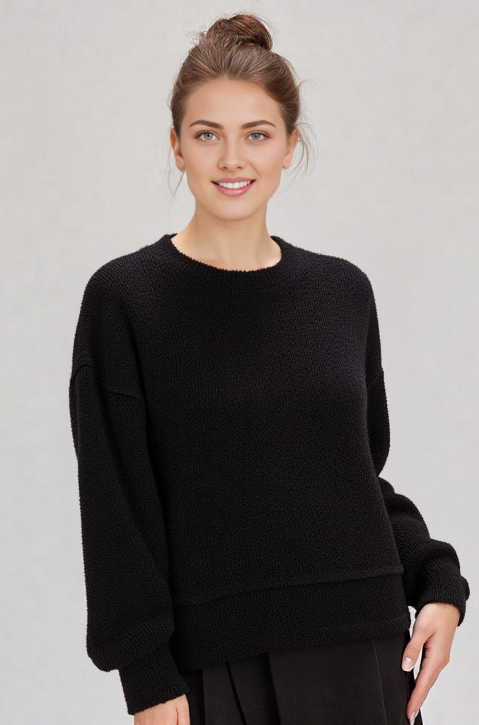 Woman in a black round-neck textured knit oversized top with drop shoulders and long sleeves, relaxed fit.”