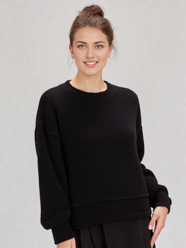 Woman in a black round-neck textured knit oversized top with drop shoulders and long sleeves, relaxed fit.”