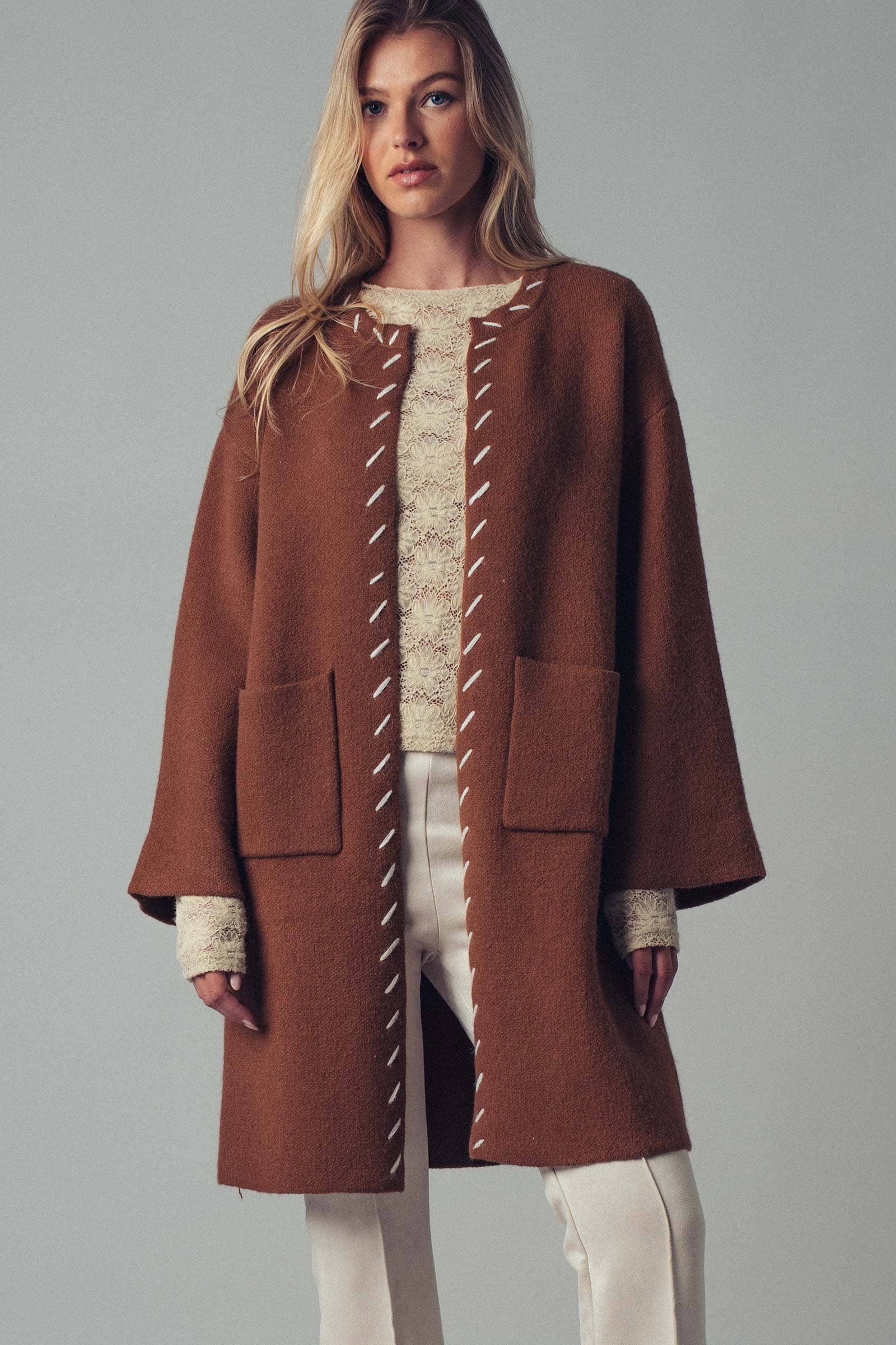 Woman wearing a brown open coat with white bold stitching trim