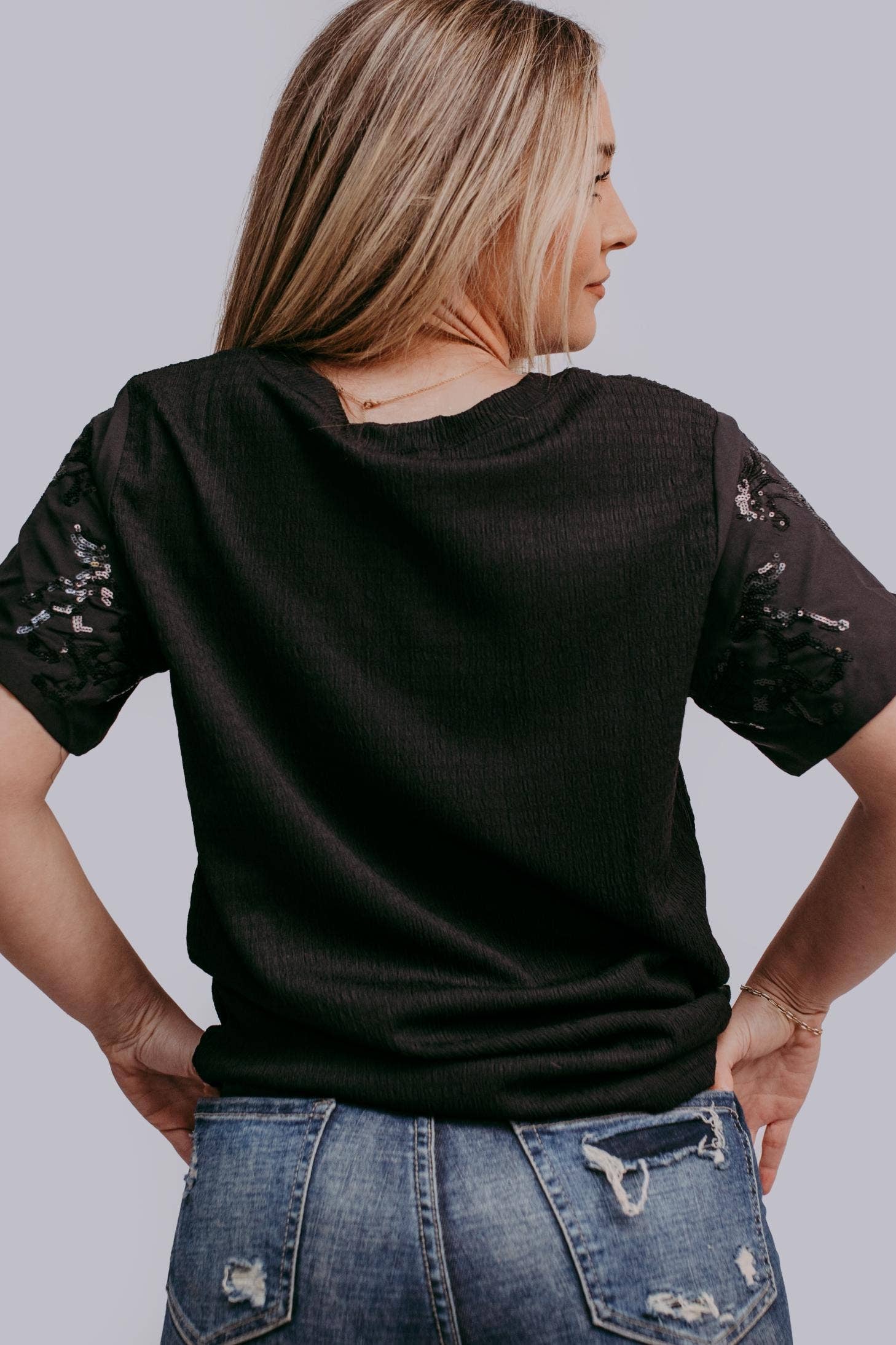Woman wearing a black t-shirt with horse sequins on a plain background