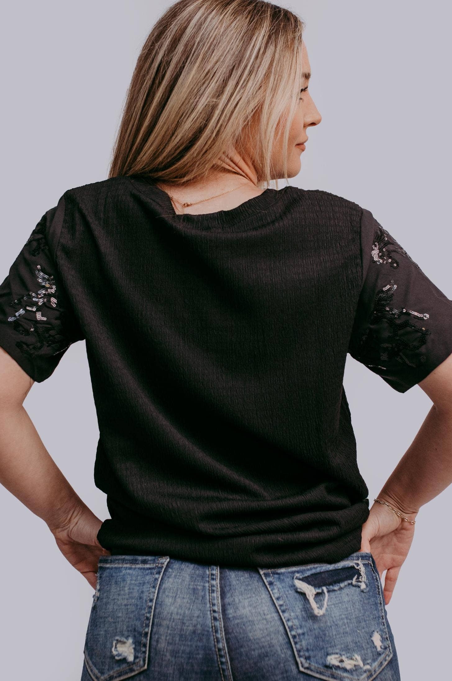 Woman wearing a black t-shirt with horse sequins on a plain background