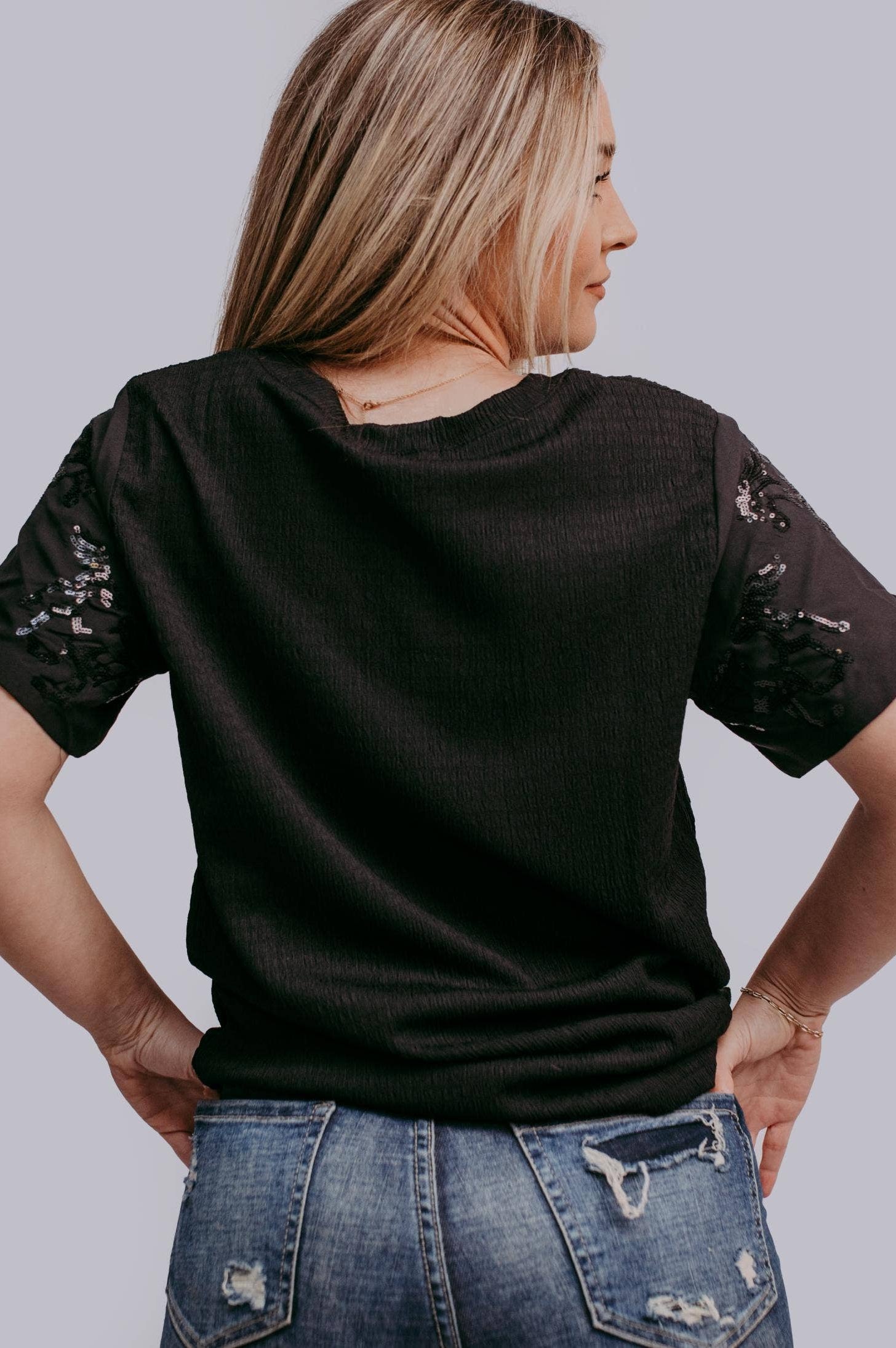 Woman wearing a black t-shirt with horse sequins on a plain background