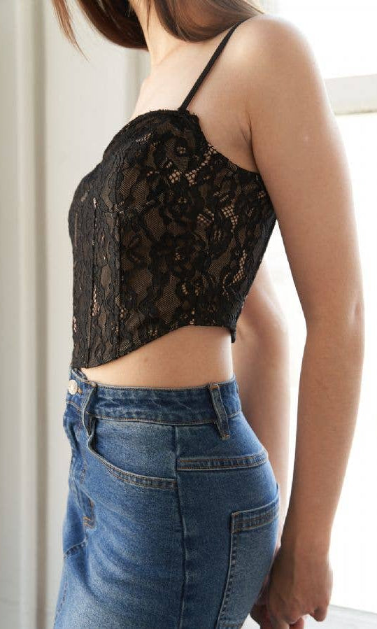 Person wearing a black lace top and blue jeans indoors.