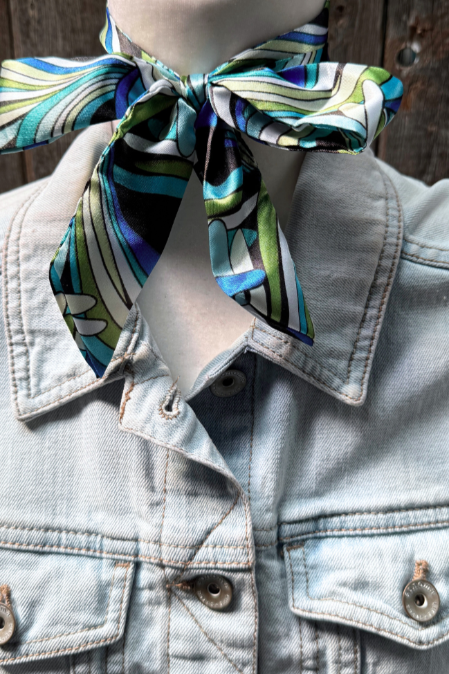 Mannequin wearing a light blue denim jacket with a colorful scarf tied around its neck against a wooden background.
