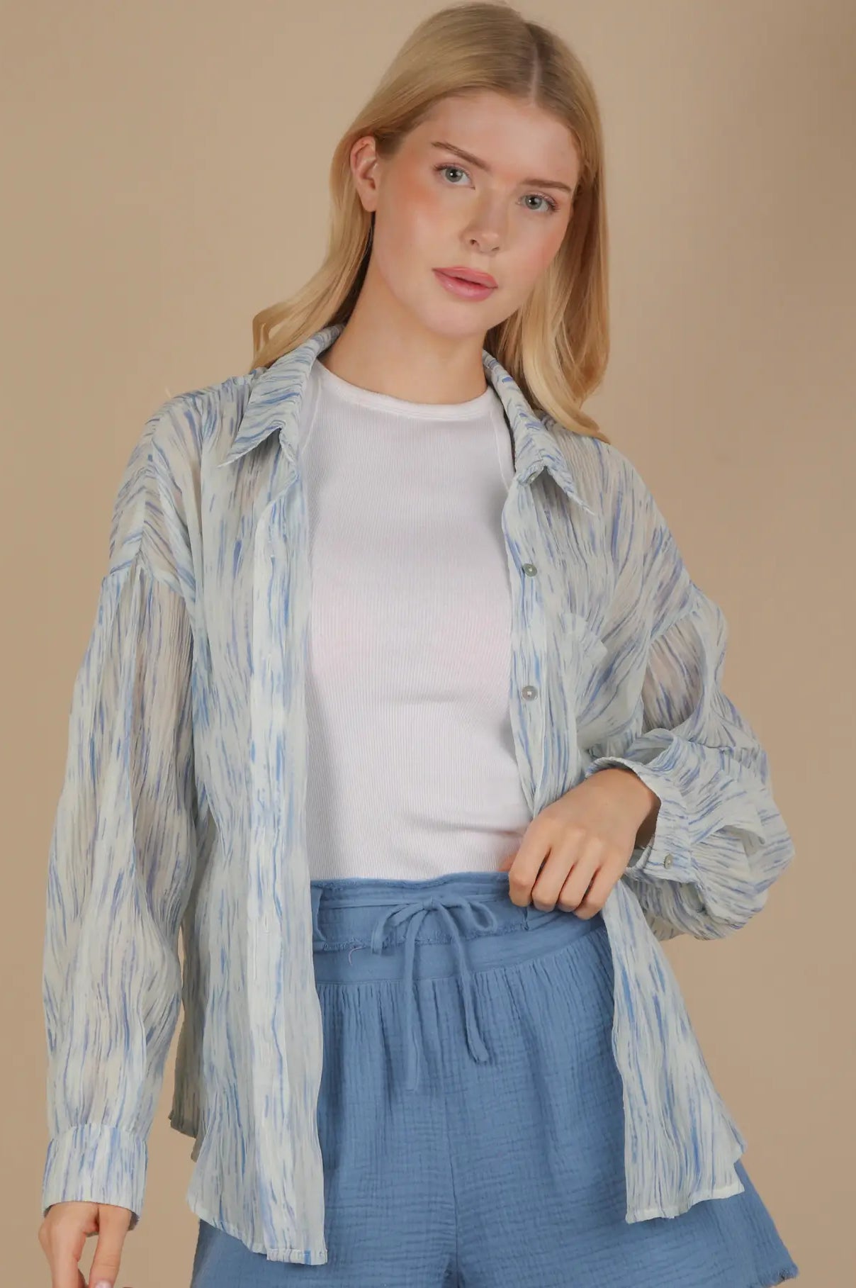 Front view of an oversized sky-blue brushstroke pleated button-down on model, showing drop shoulder, button cuff, and flowing crinkle texture.