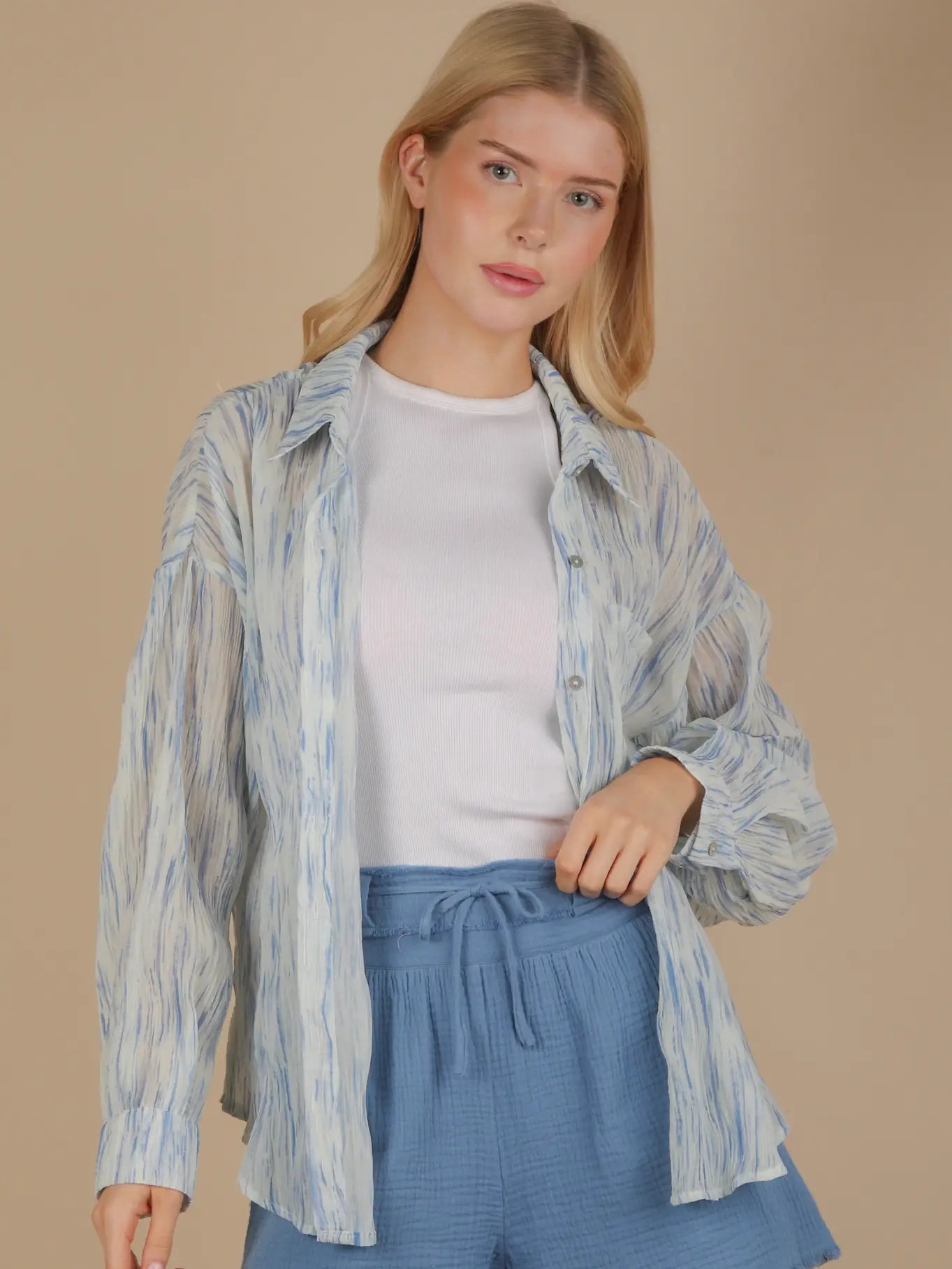 Front view of an oversized sky-blue brushstroke pleated button-down on model, showing drop shoulder, button cuff, and flowing crinkle texture.