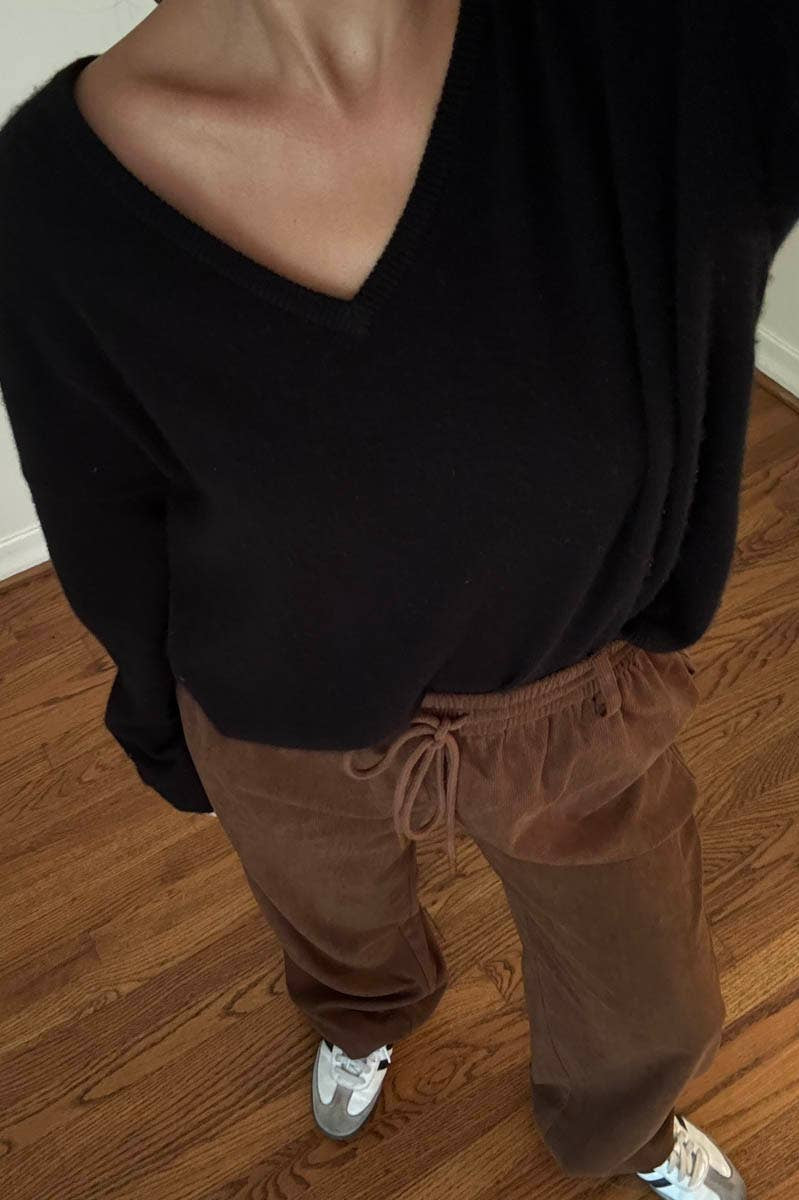 Person wearing a black top and brown pants on a wooden floor.