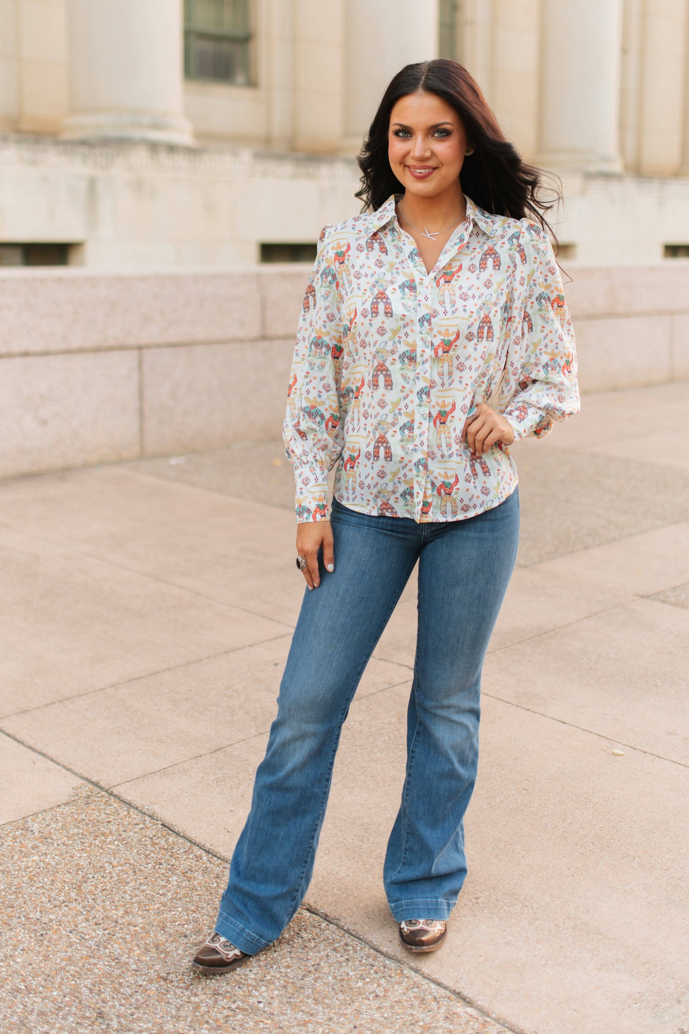 Woman wearing a patterned blouse and blue jeans standing on a stone pavement.