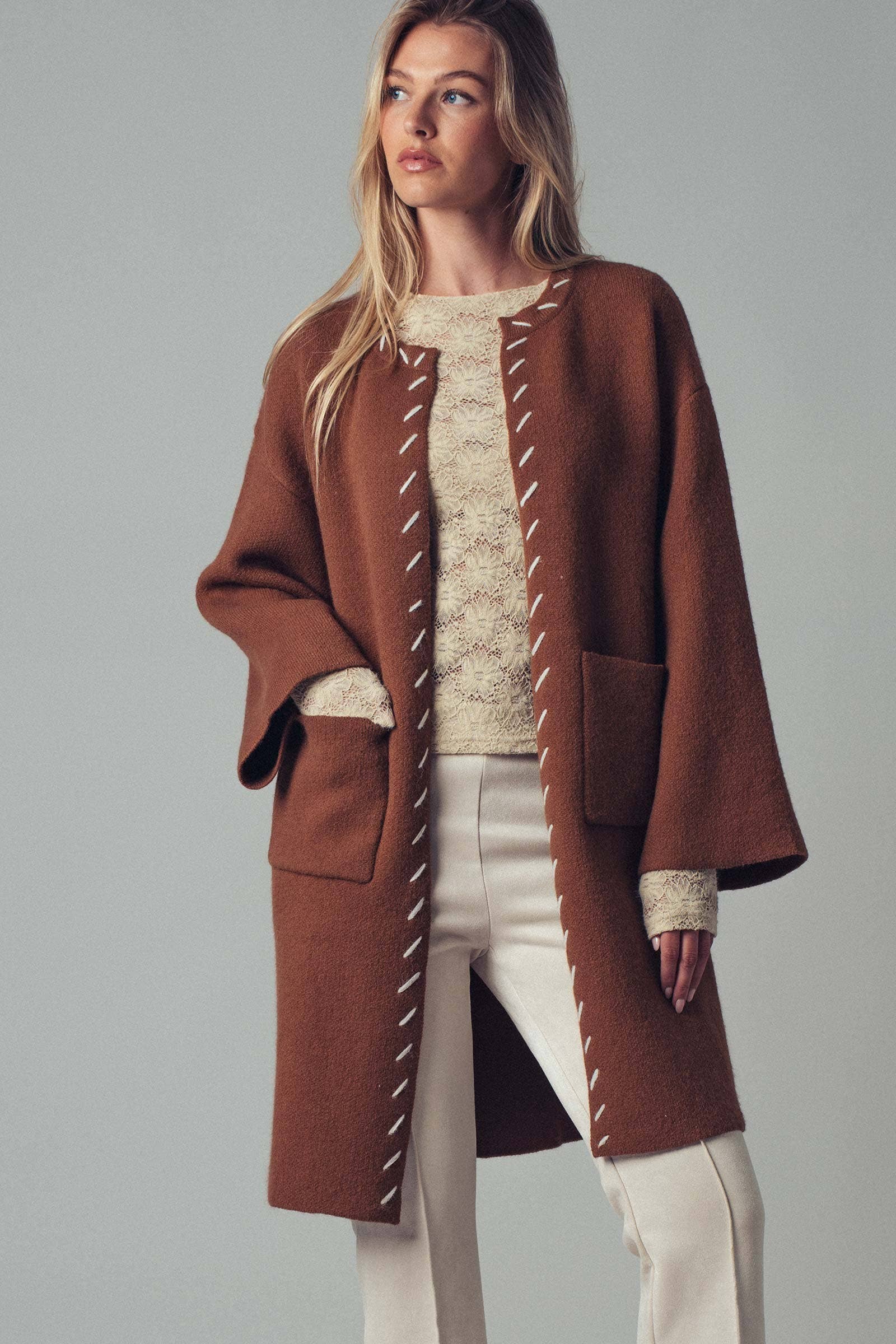 Woman wearing a brown open coat with white bold stitching trim on a background