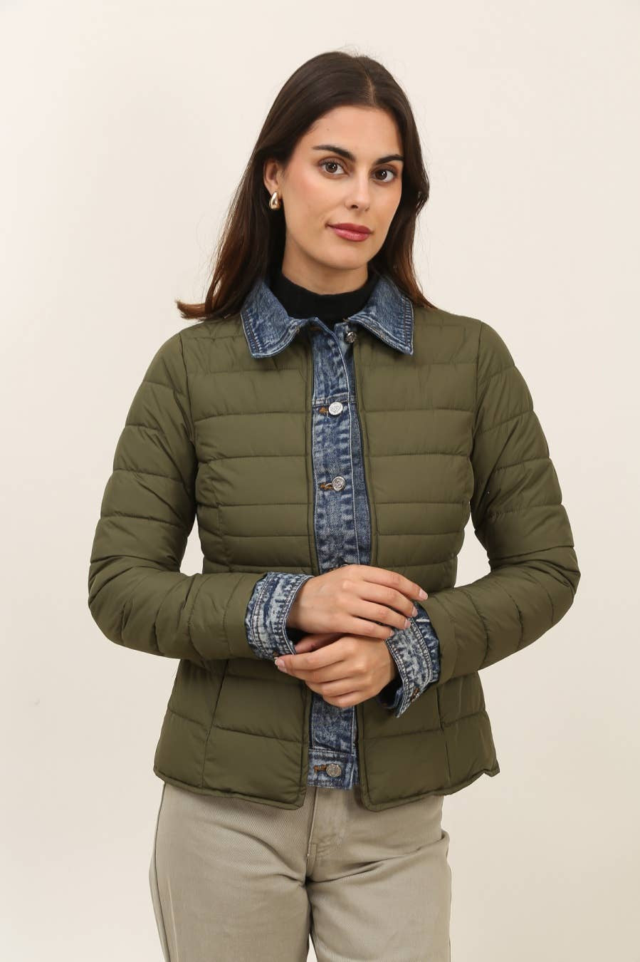 Woman wearing a green puffer jacket with denim collar and cuffs on a beige background
