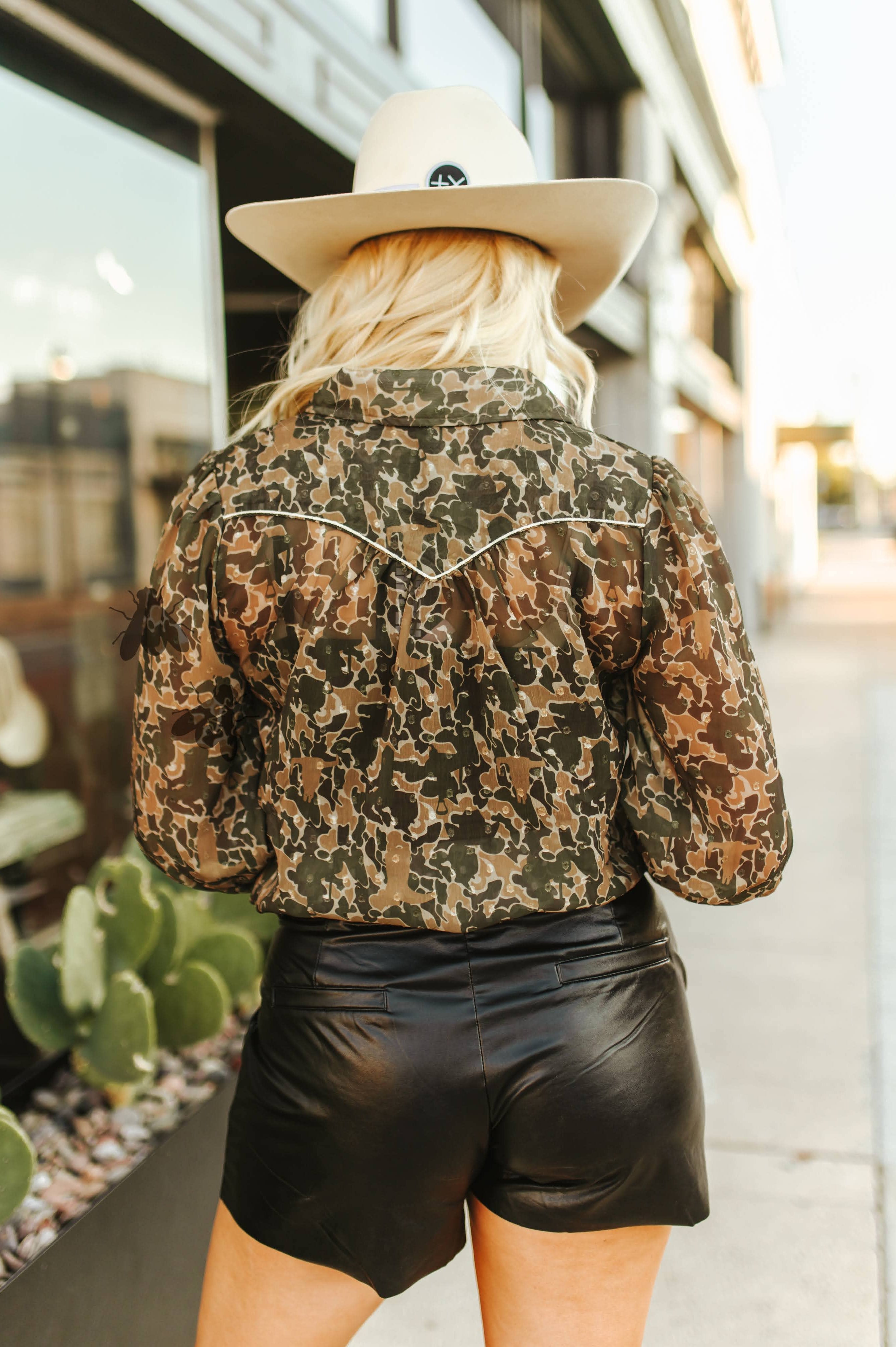 Person wearing a camouflage jacket and black shorts with a hat, standing outdoors.
