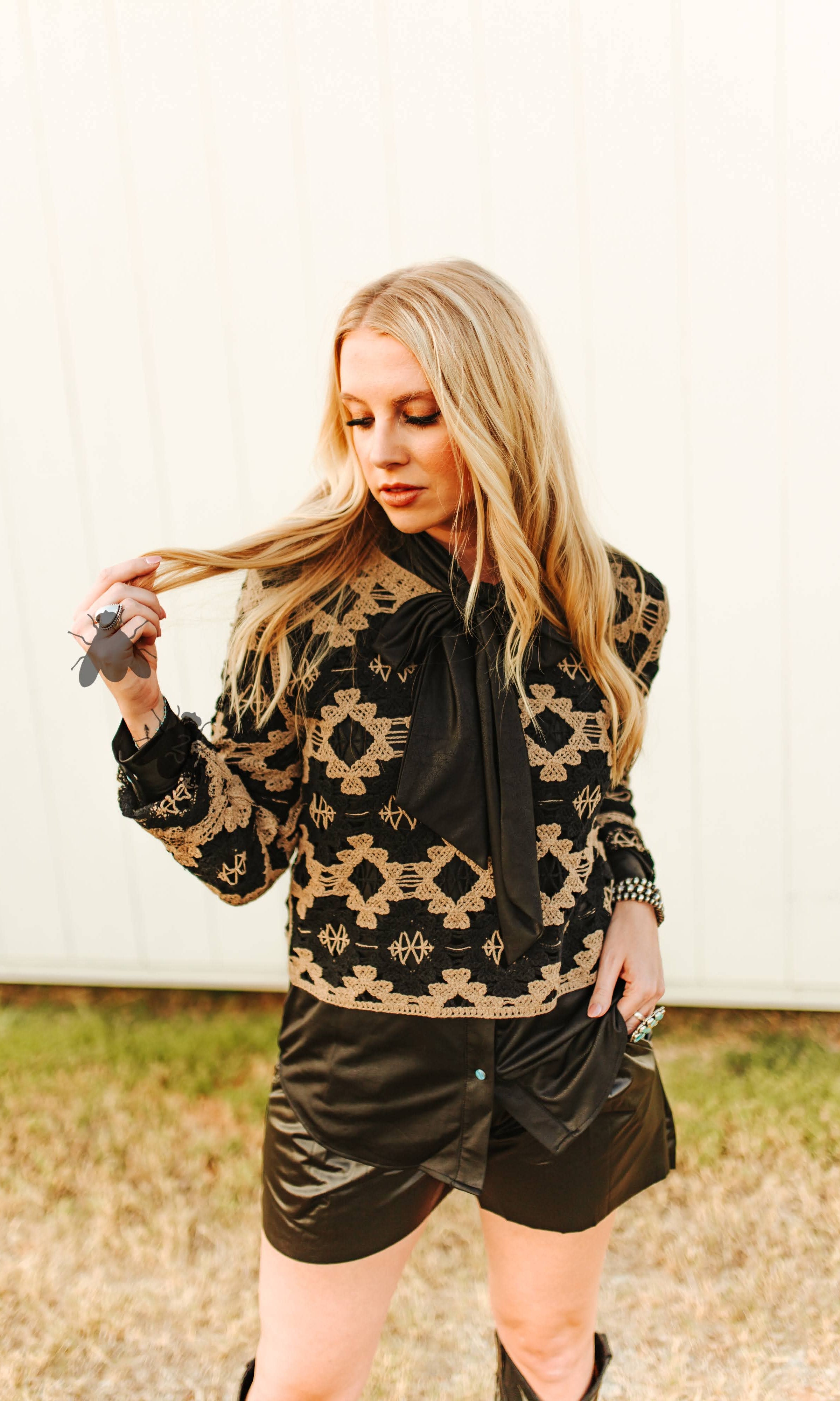 Woman wearing a black and gold patterned jacket with leather shorts outdoors.