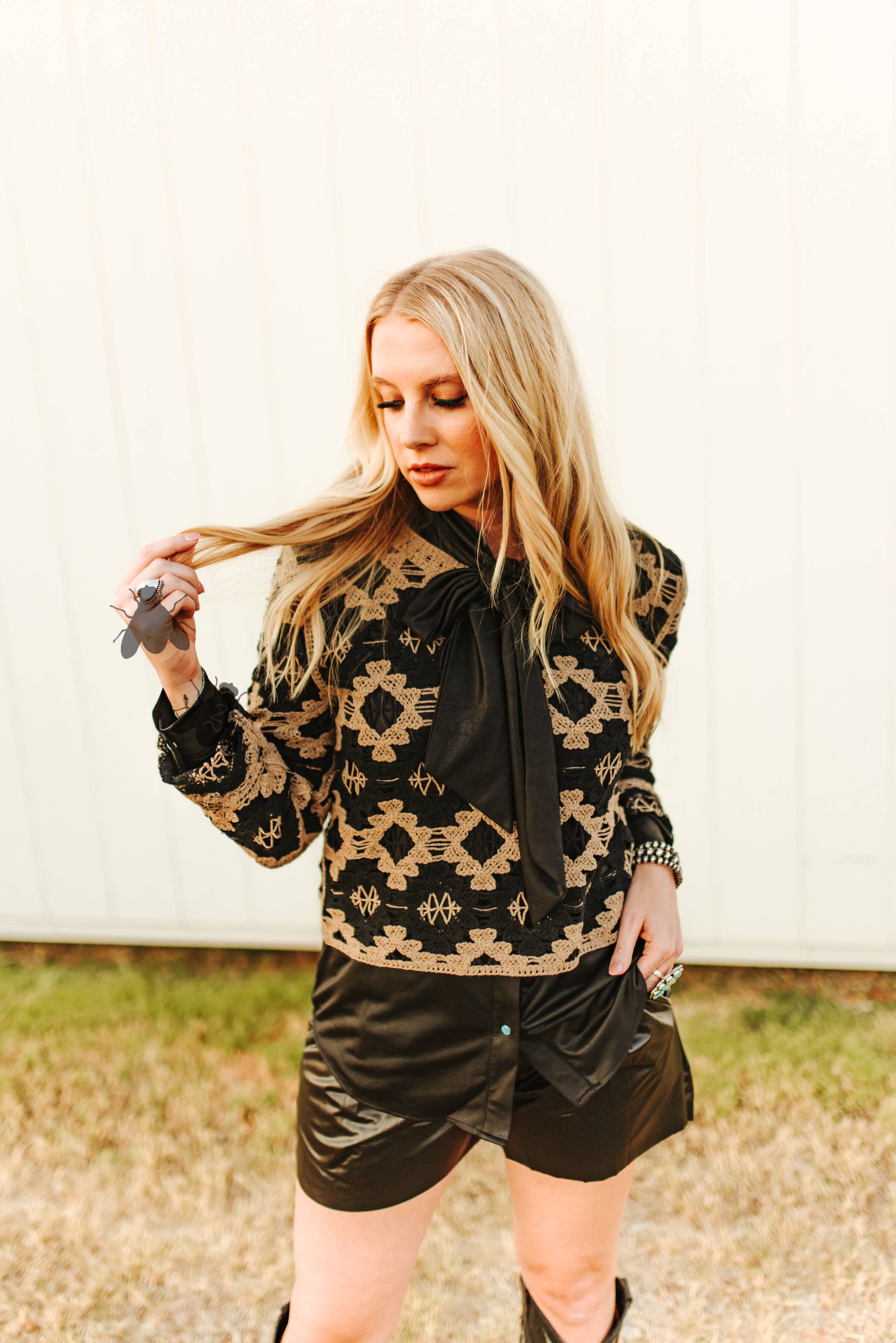 Woman wearing a black and gold patterned jacket with leather shorts outdoors.