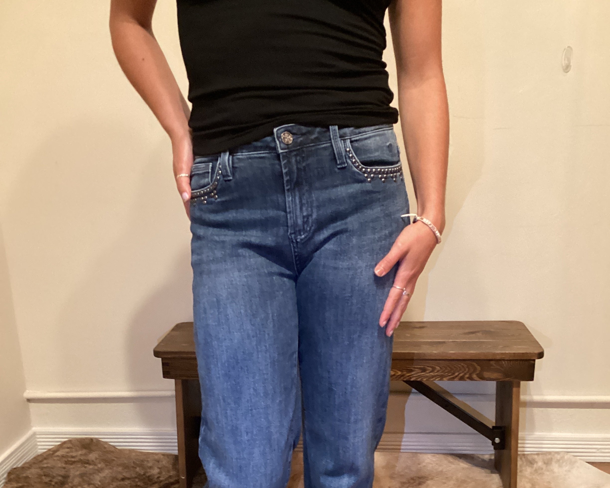 Person wearing blue jeans with stud detailing on the edge of the front pockets