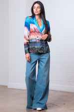Woman wearing a colorful blazer and blue pants against a white background
