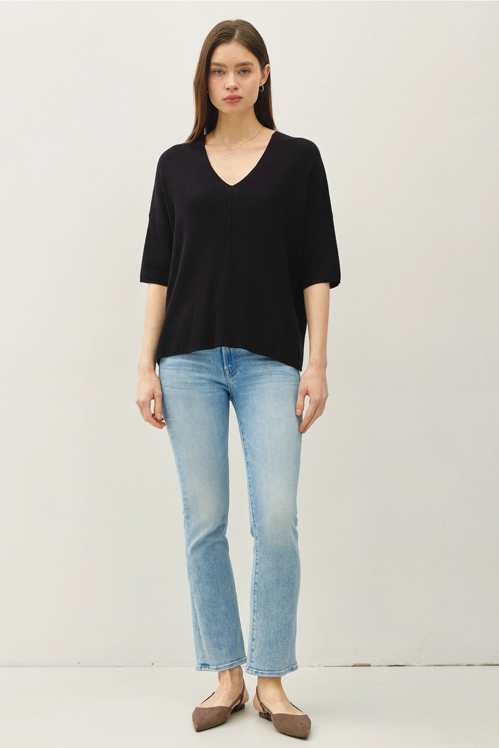 Woman wearing a black top and light blue jeans on a white background