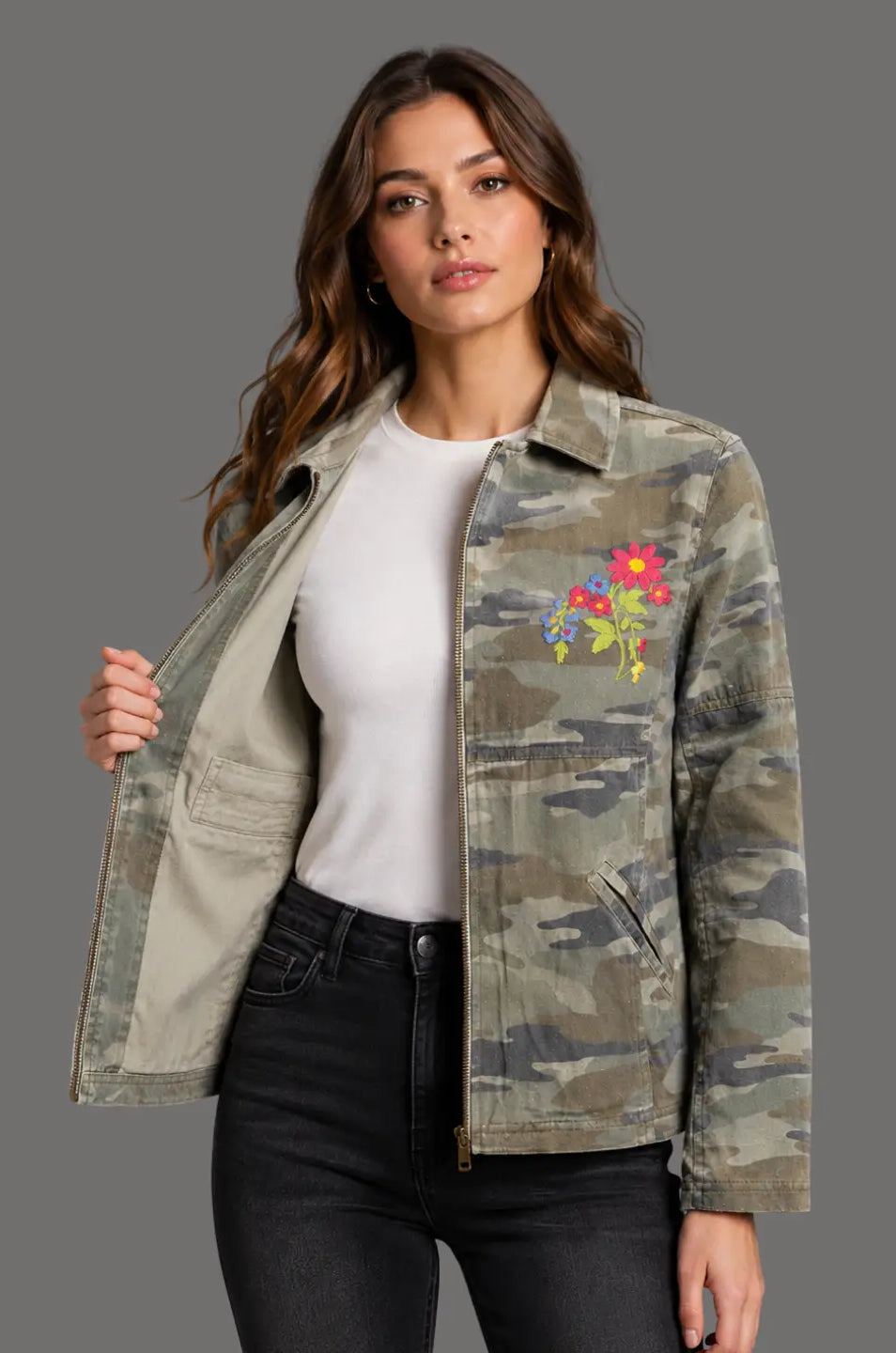 Woman wearing a camouflage jacket with floral embroidery on a gray background
