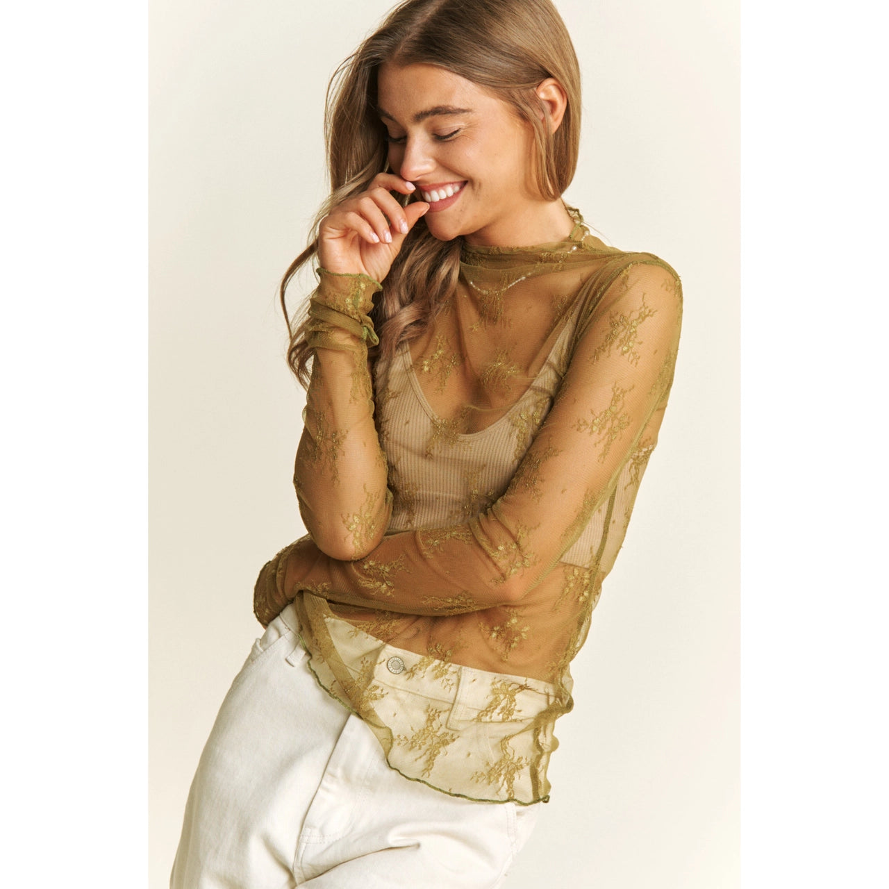 Woman wearing a sheer olive top with lace details on a plain background