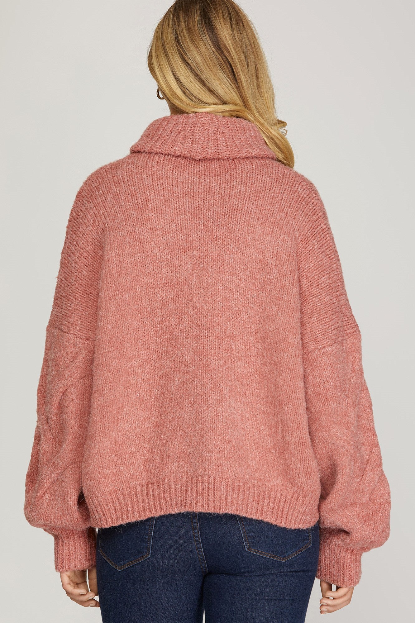 Back view of rosy-rust cable knit turtleneck sweater with ribbed cuffs and hem.
