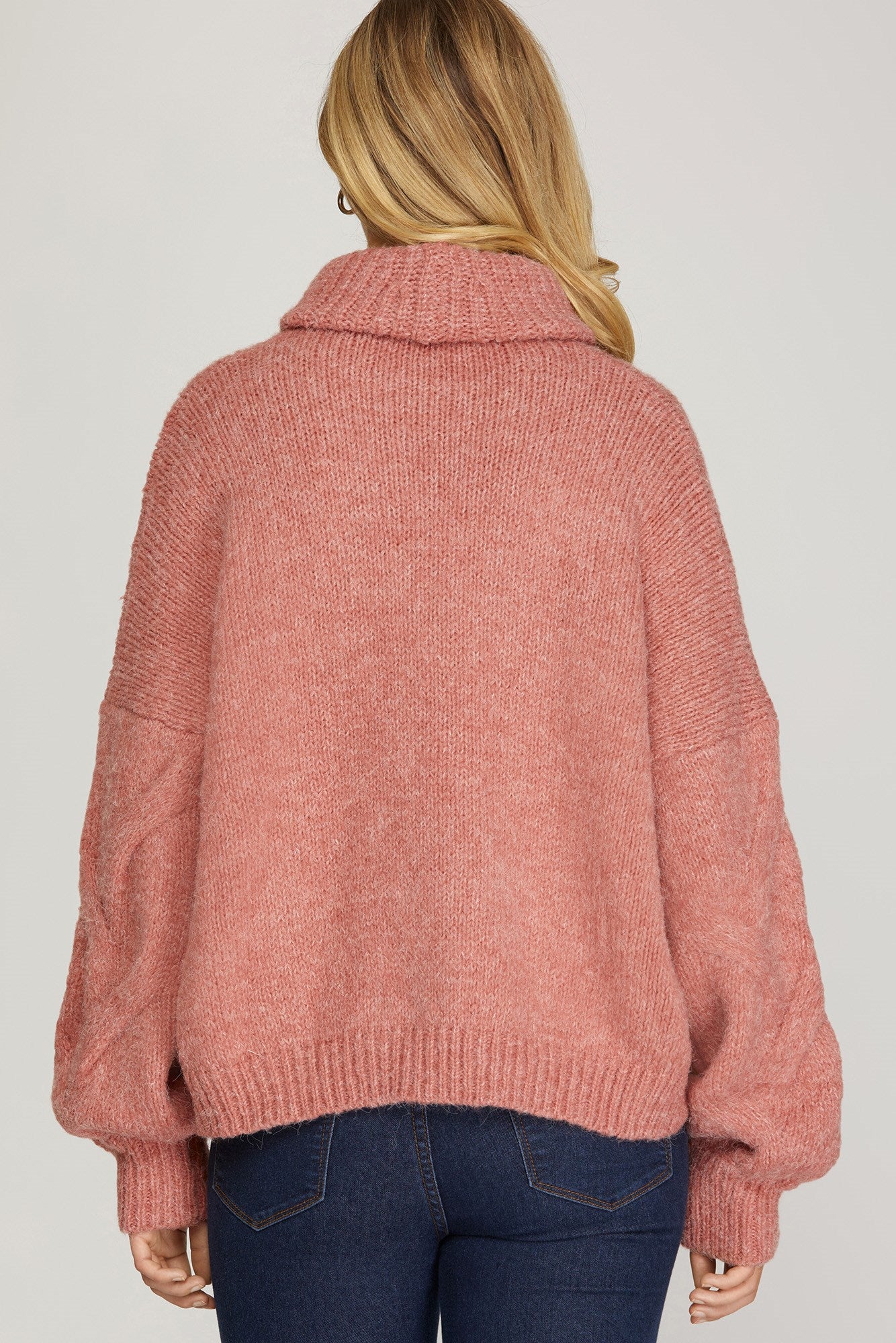 Back view of rosy-rust cable knit turtleneck sweater with ribbed cuffs and hem.
