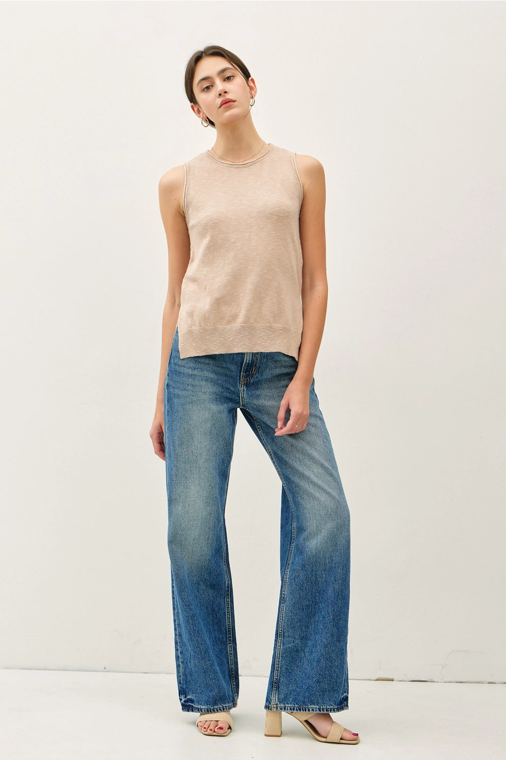Woman wearing a beige sleeveless top and blue jeans on a white background