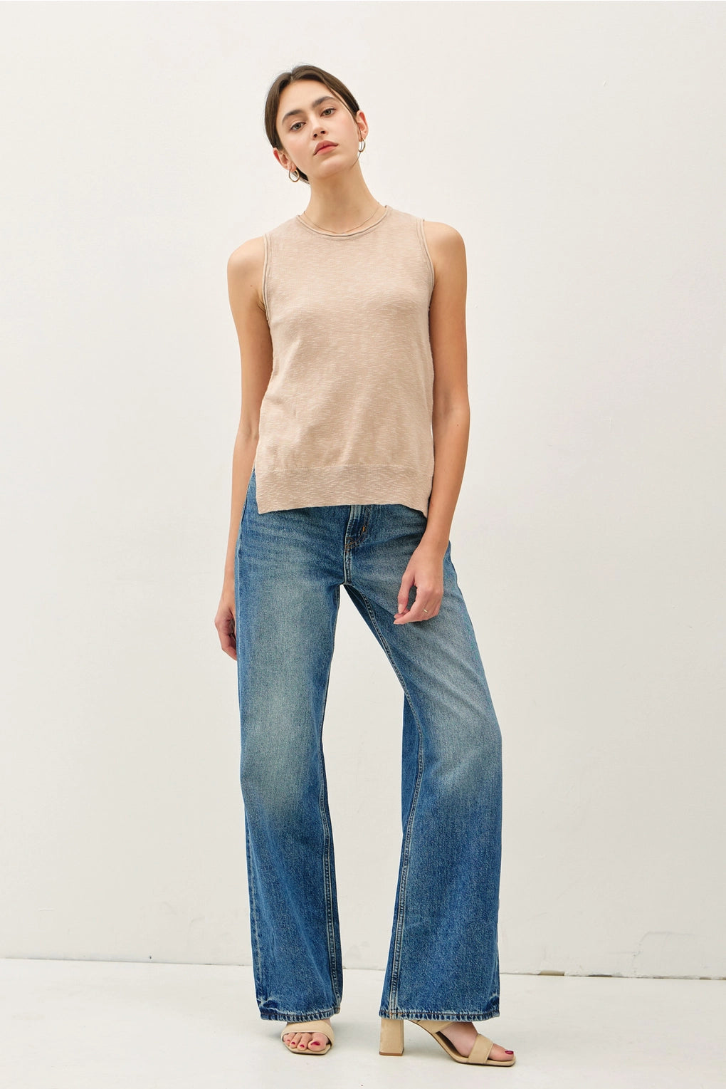 Woman wearing a beige sleeveless top and blue jeans on a white background