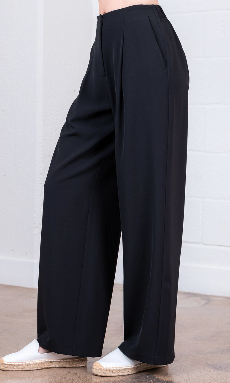 Black wide-leg pants worn by a person against a white brick wall.