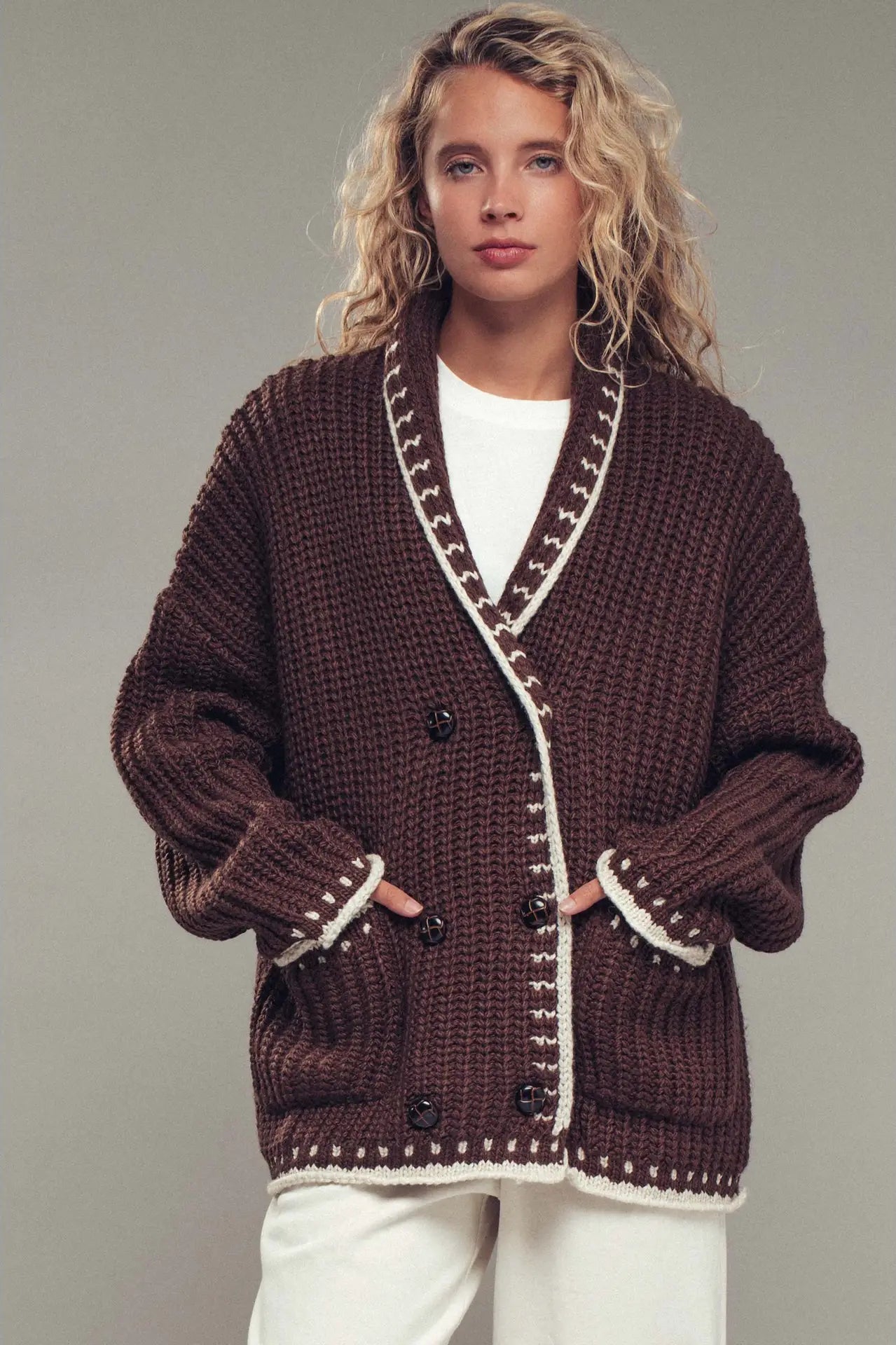Woman wearing a brown knitted cardigan with white trim on a plain background