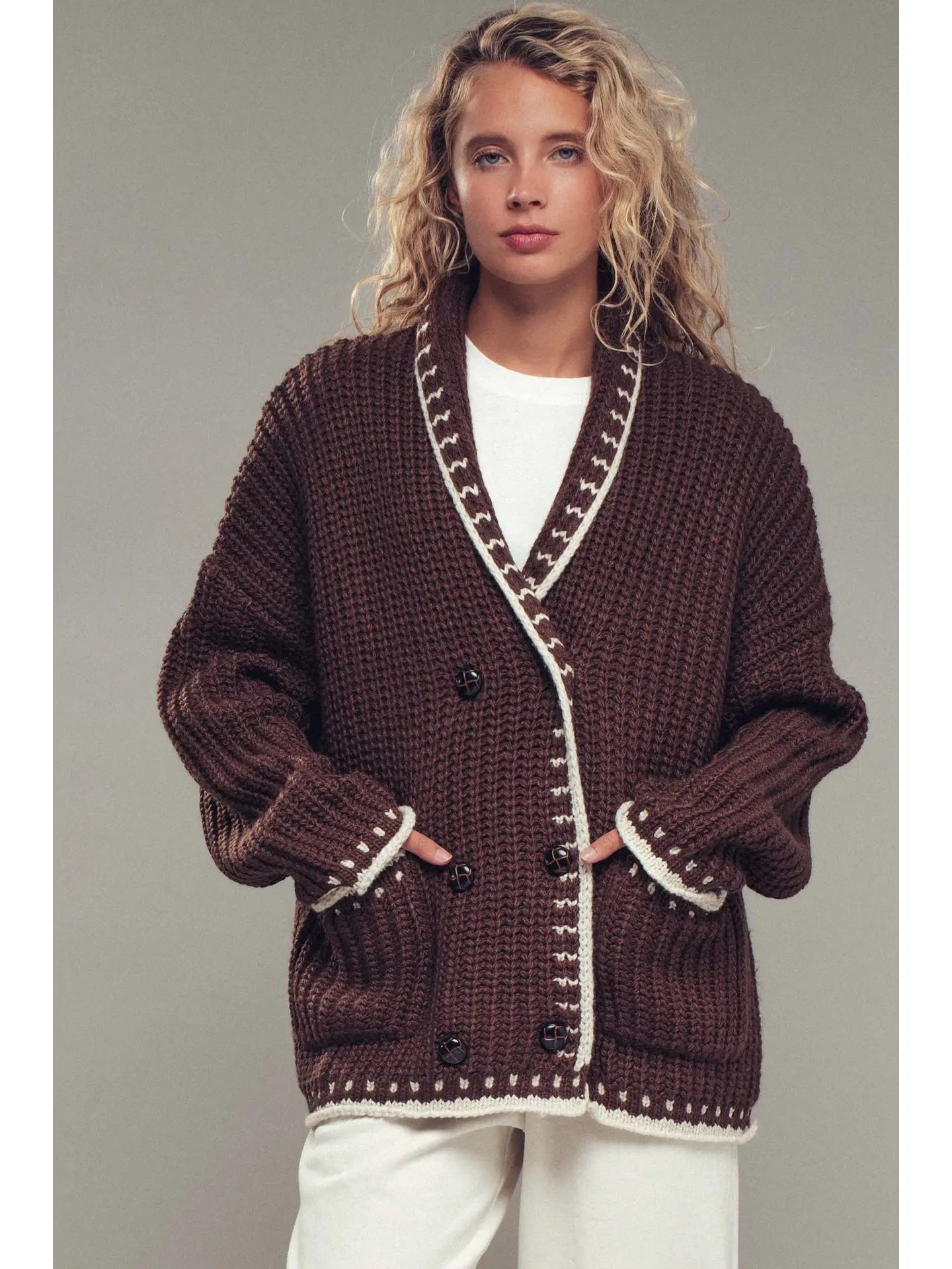 Woman wearing a brown knitted cardigan with white trim on a plain background