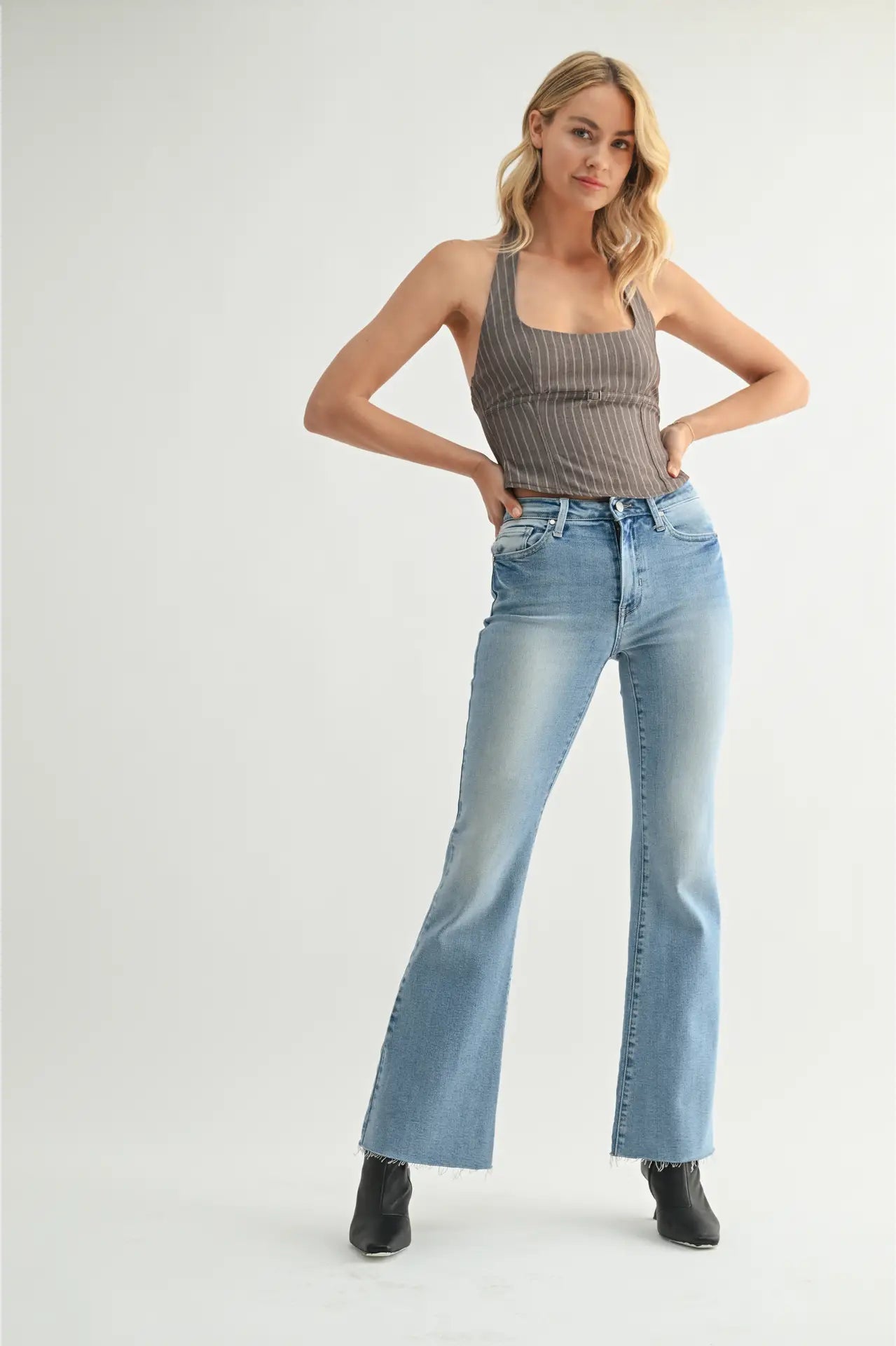 Woman wearing a ribbed tank top and light blue jeans on a white background