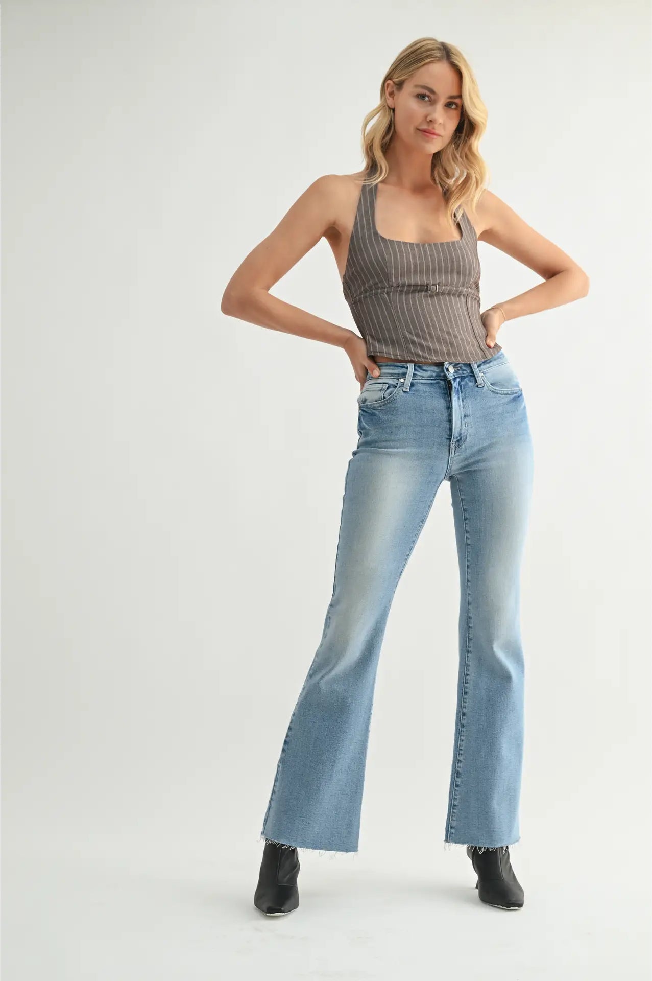 Woman wearing a ribbed tank top and light blue jeans on a white background