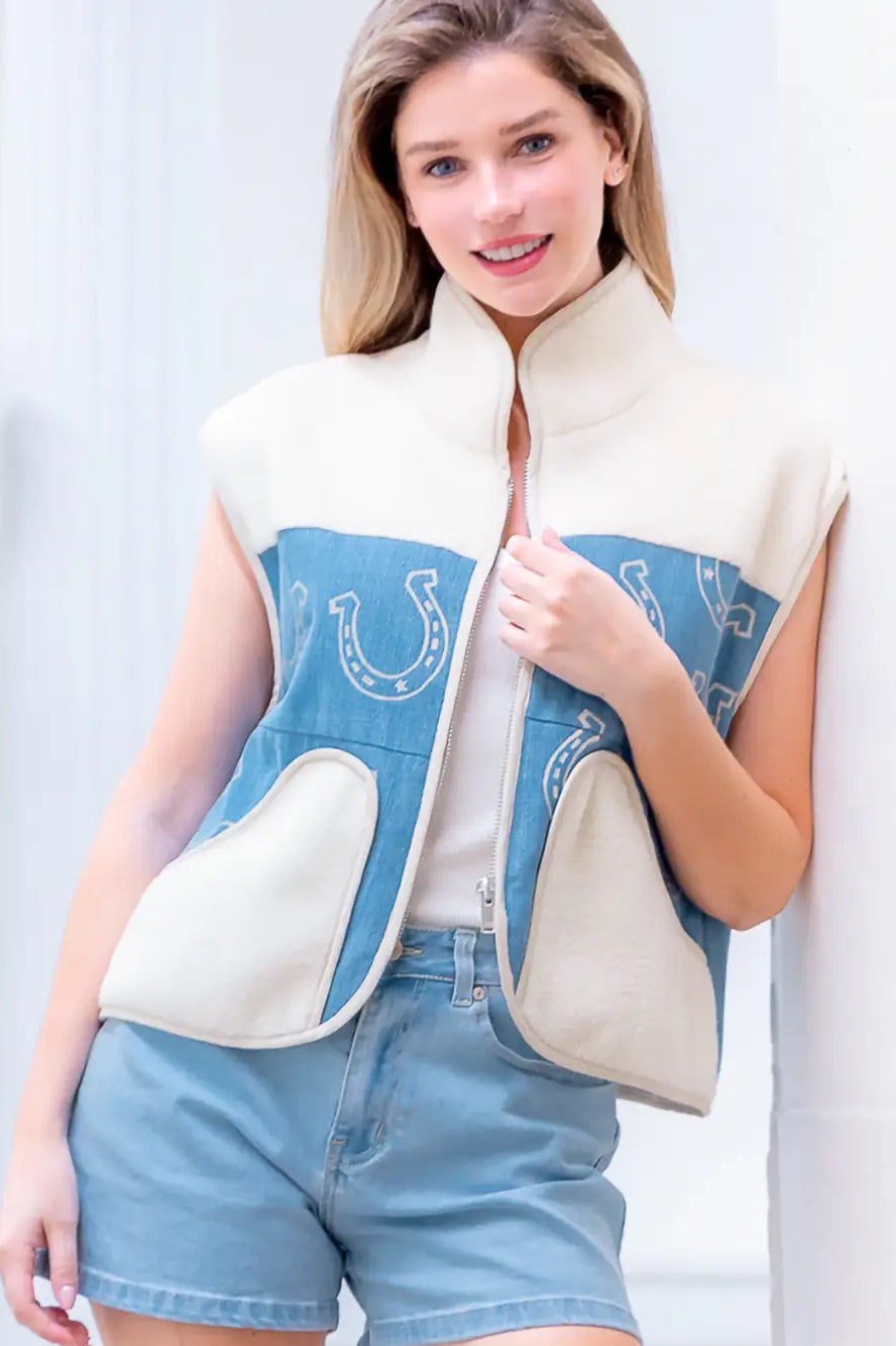 Model wearing indigo denim vest with white horseshoe print and faux-fur collar, zipped front, hands in pockets.”