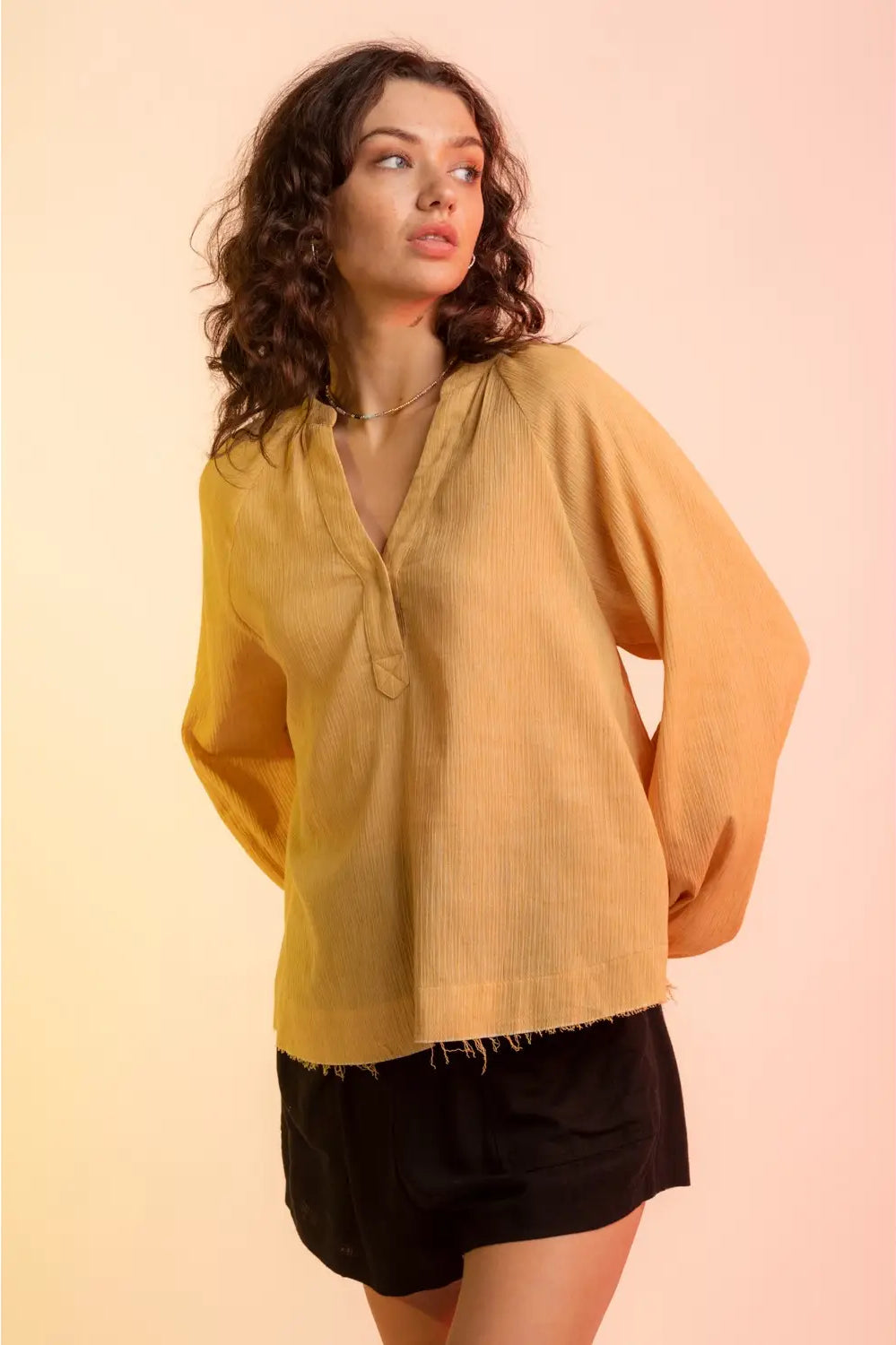 Model wearing yellow gauze V-neck blouse with raglan bubble sleeves and raw hem,