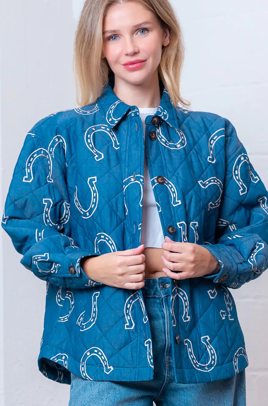 Front view of denim-blue quilted jacket with white horseshoe print and button front on model.
