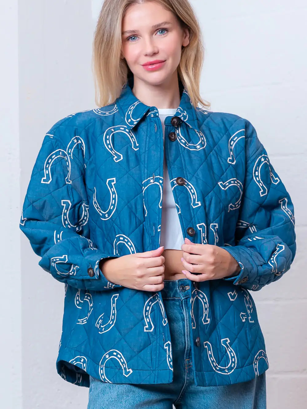 Front view of denim-blue quilted jacket with white horseshoe print and button front on model.