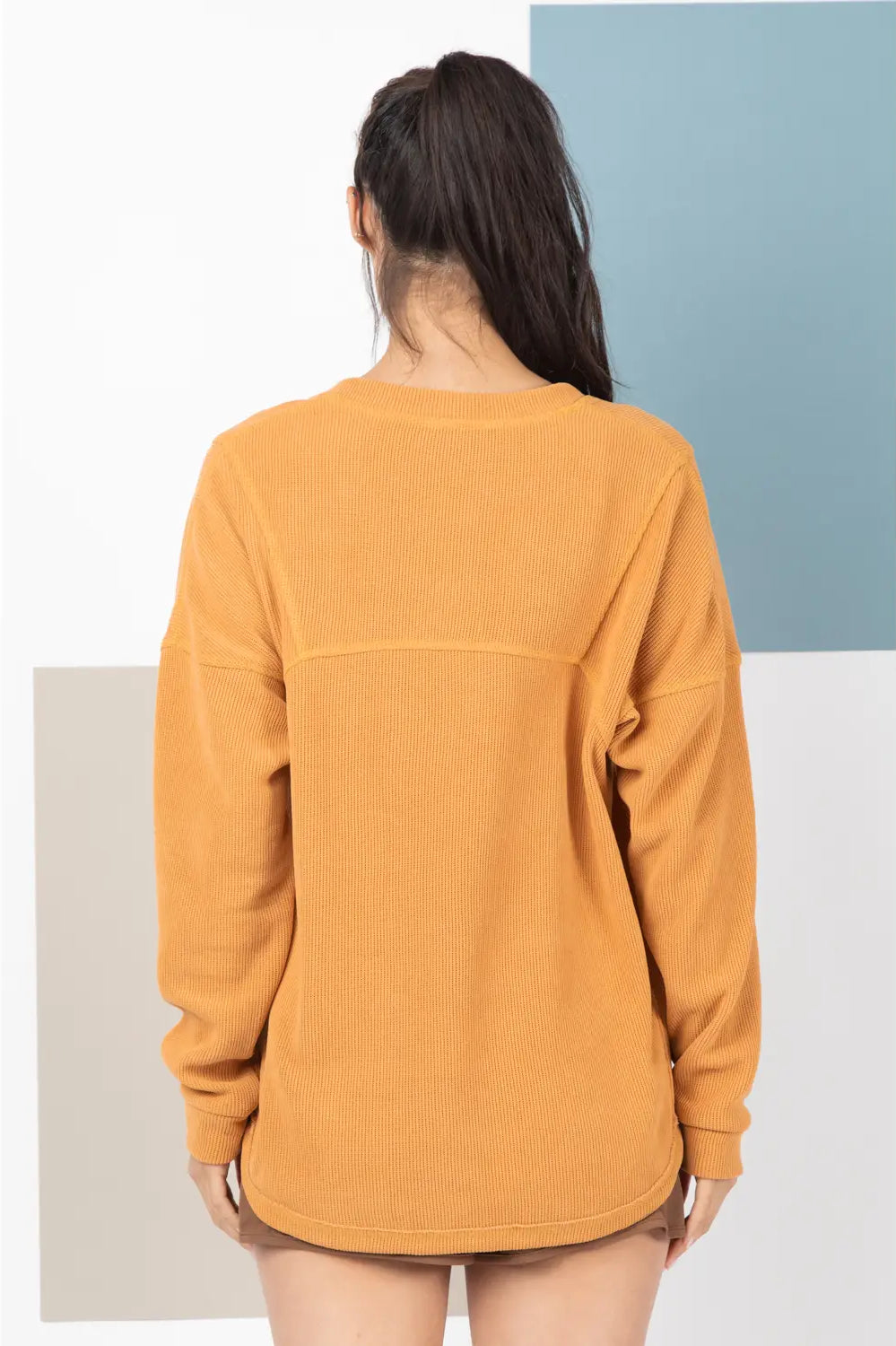 Person wearing a mustard yellow sweatshirt against a minimalistic background