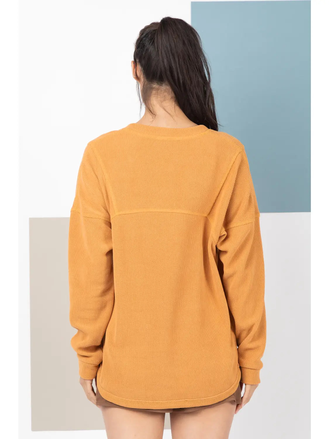 Person wearing a mustard yellow sweatshirt against a minimalistic background