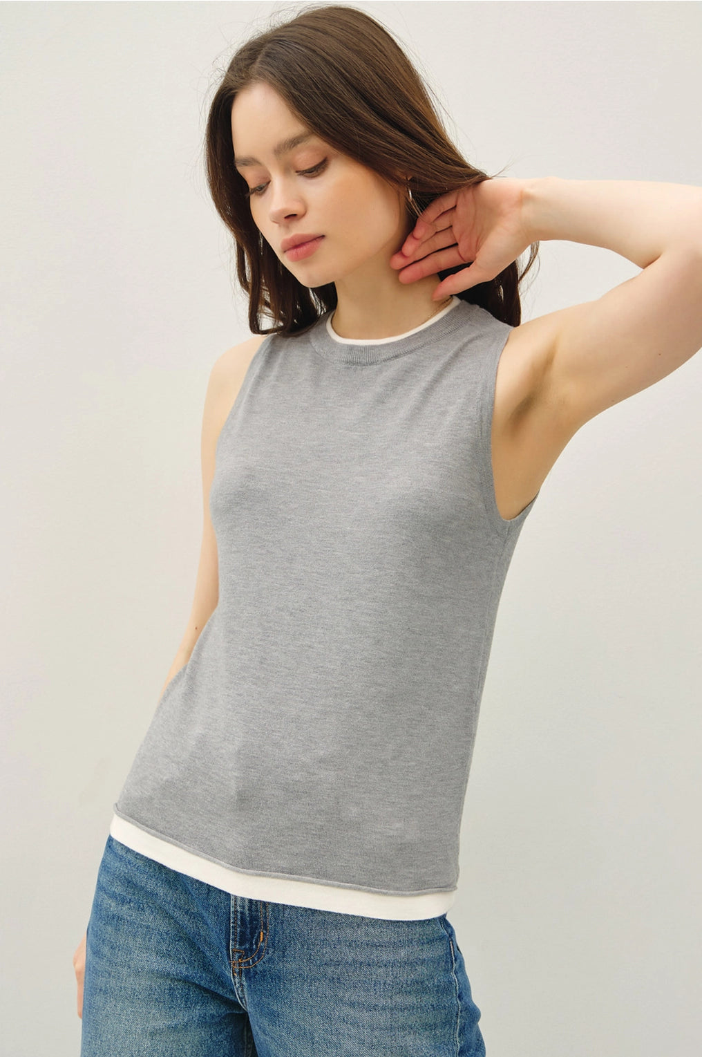 Woman wearing a gray tank top and blue jeans against a plain background