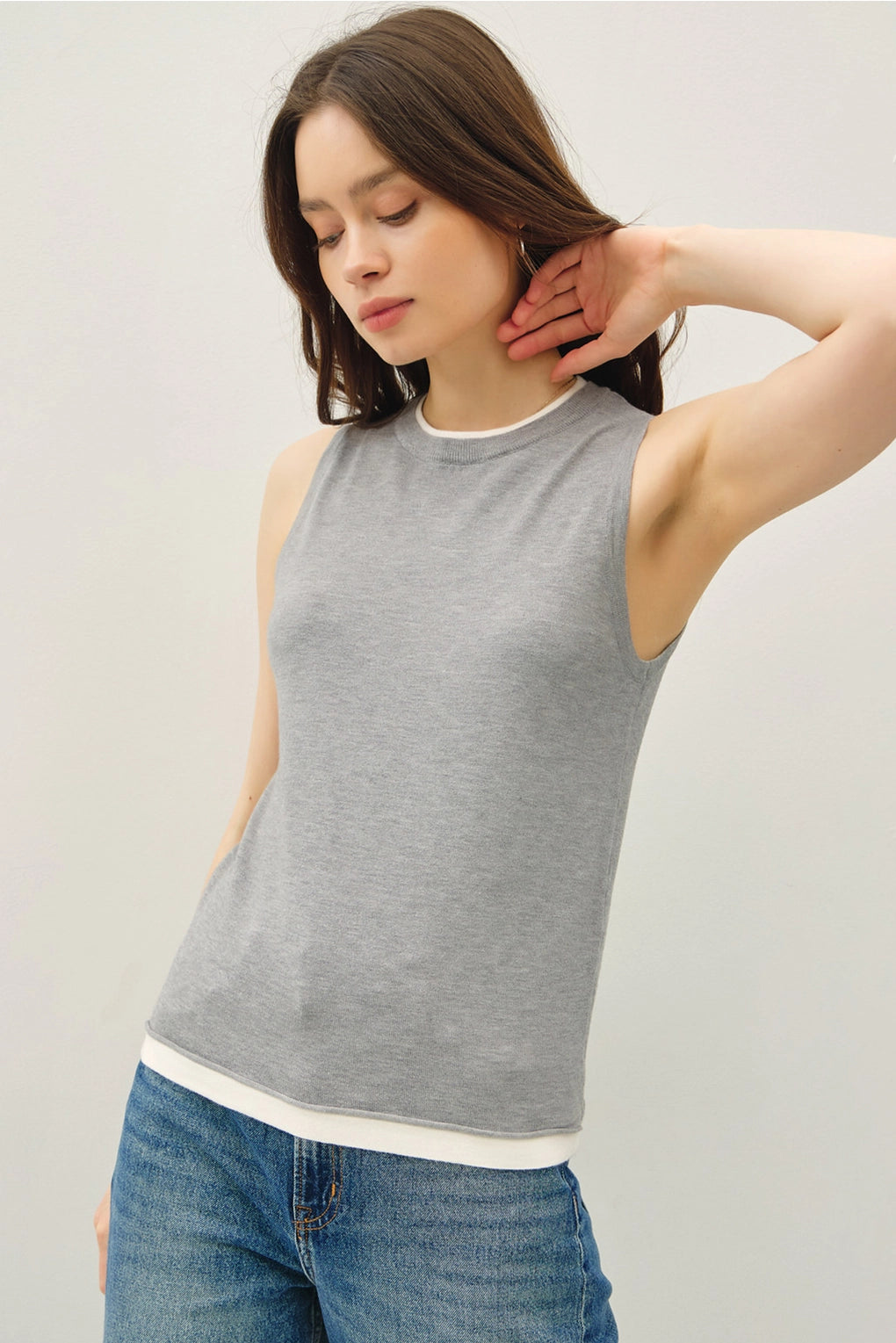 Woman wearing a gray tank top and blue jeans against a plain background