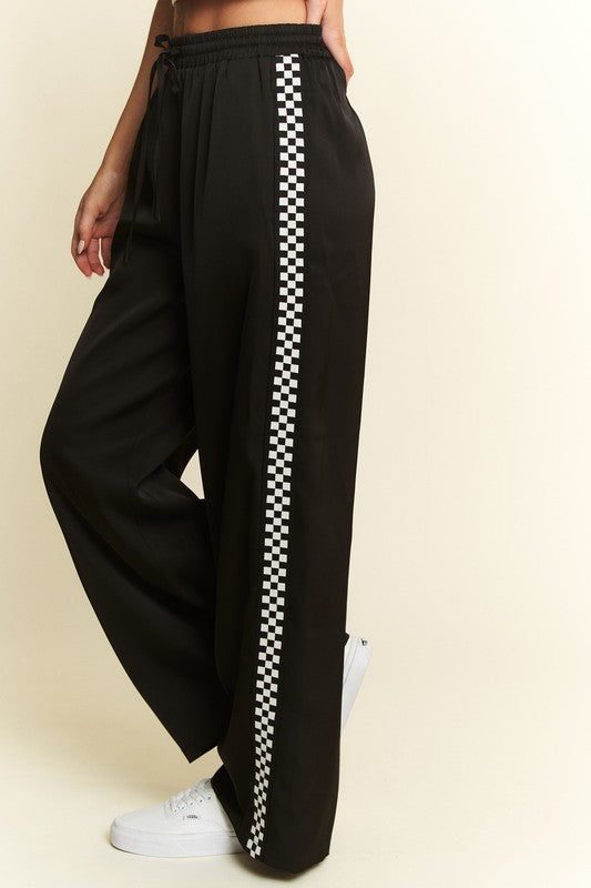Black track pants with a white checkered stripe on a beige background