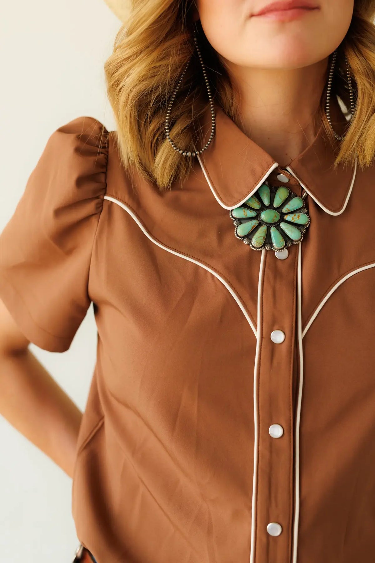 Women's brown Western pearl snap blouse featuring white contrast piping, classic Western yoke, puff sleeves, and a tailored fit.