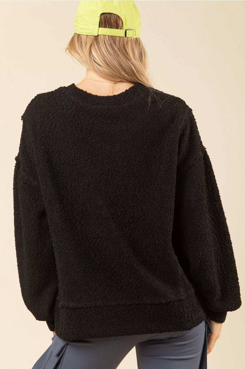 Back of black textured knit oversized top showing drop shoulders and raw-edge hem on model.”