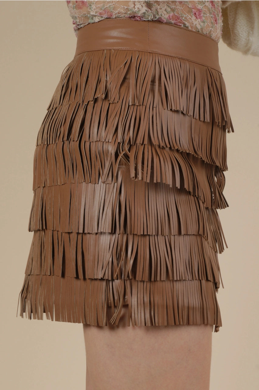 Side view of brown fringe mini skirt in vegan leather with multi-tier tassels