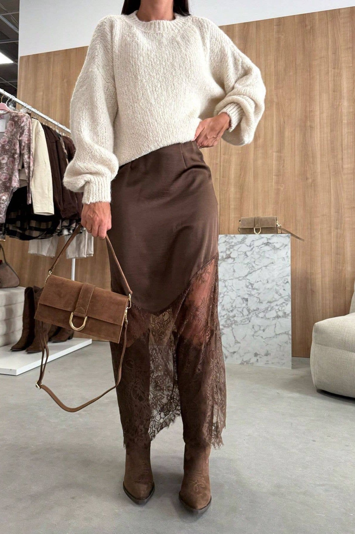 Person wearing a white sweater and brown skirt with a matching handbag in an indoor setting.