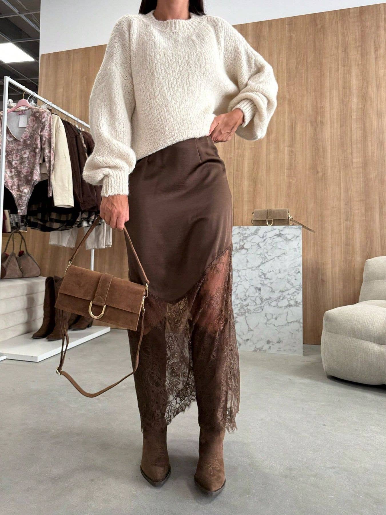Person wearing a white sweater and brown skirt with a matching handbag in an indoor setting.
