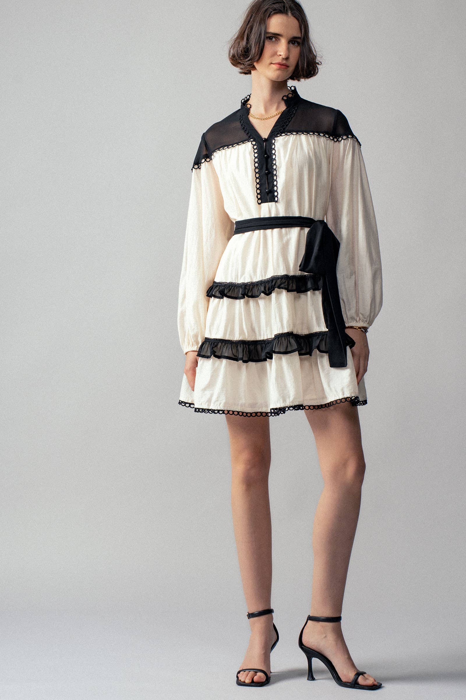 Woman wearing a white dress with black lace details on a gray background