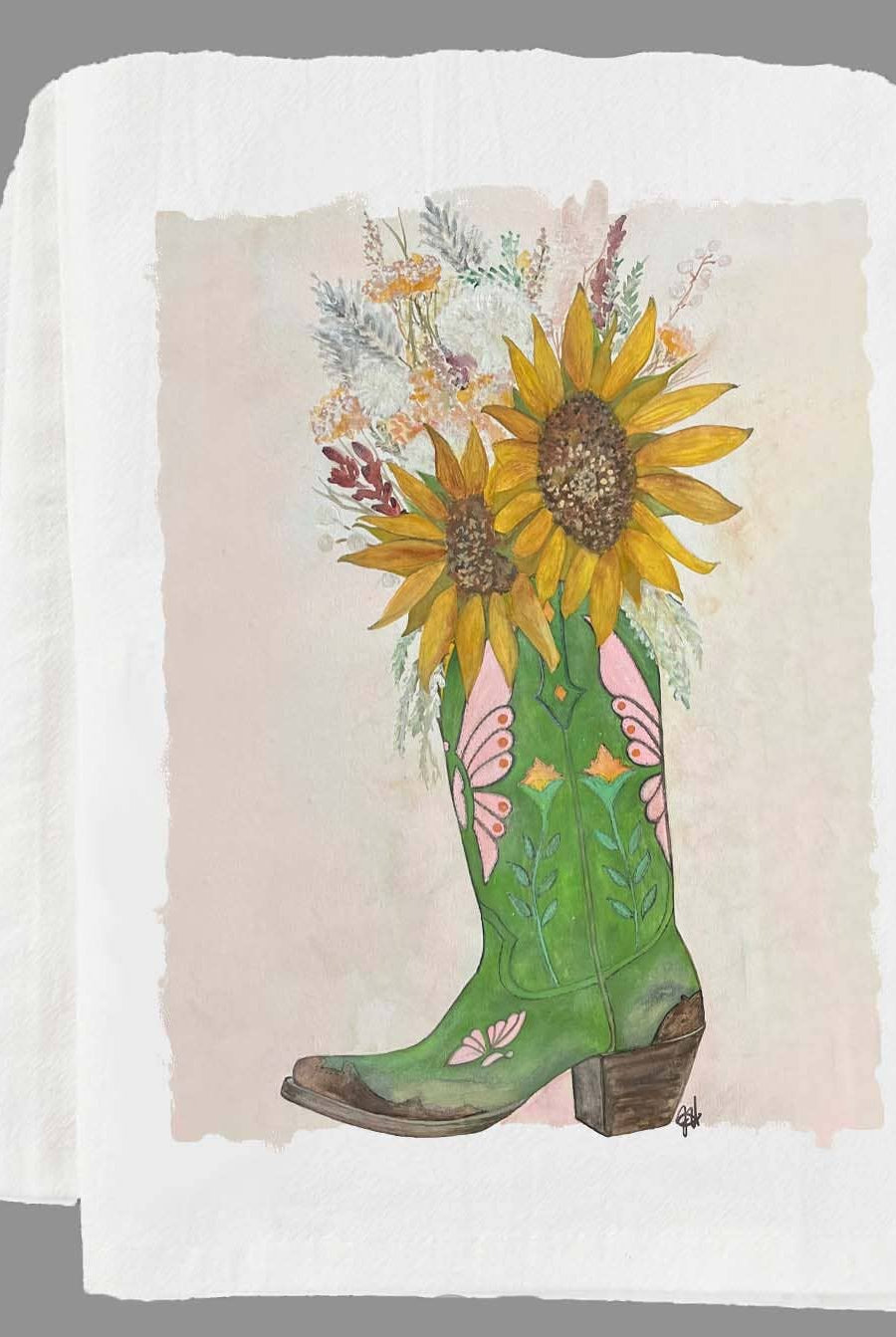 Green cowboy boot with sunflowers and floral design on a folded white tea towel.