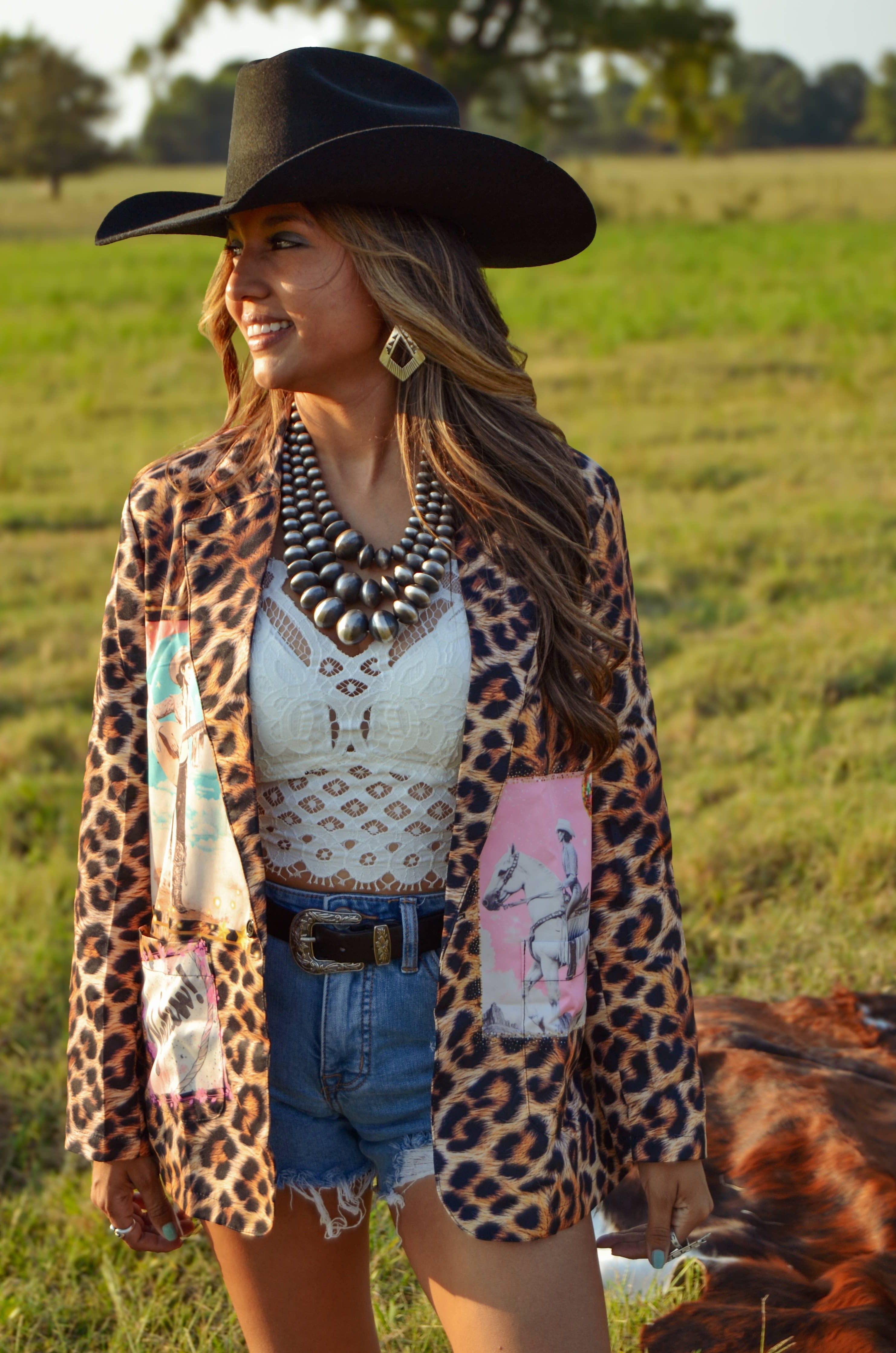 Woman in a leopard print jacket standing in a field with a cow.